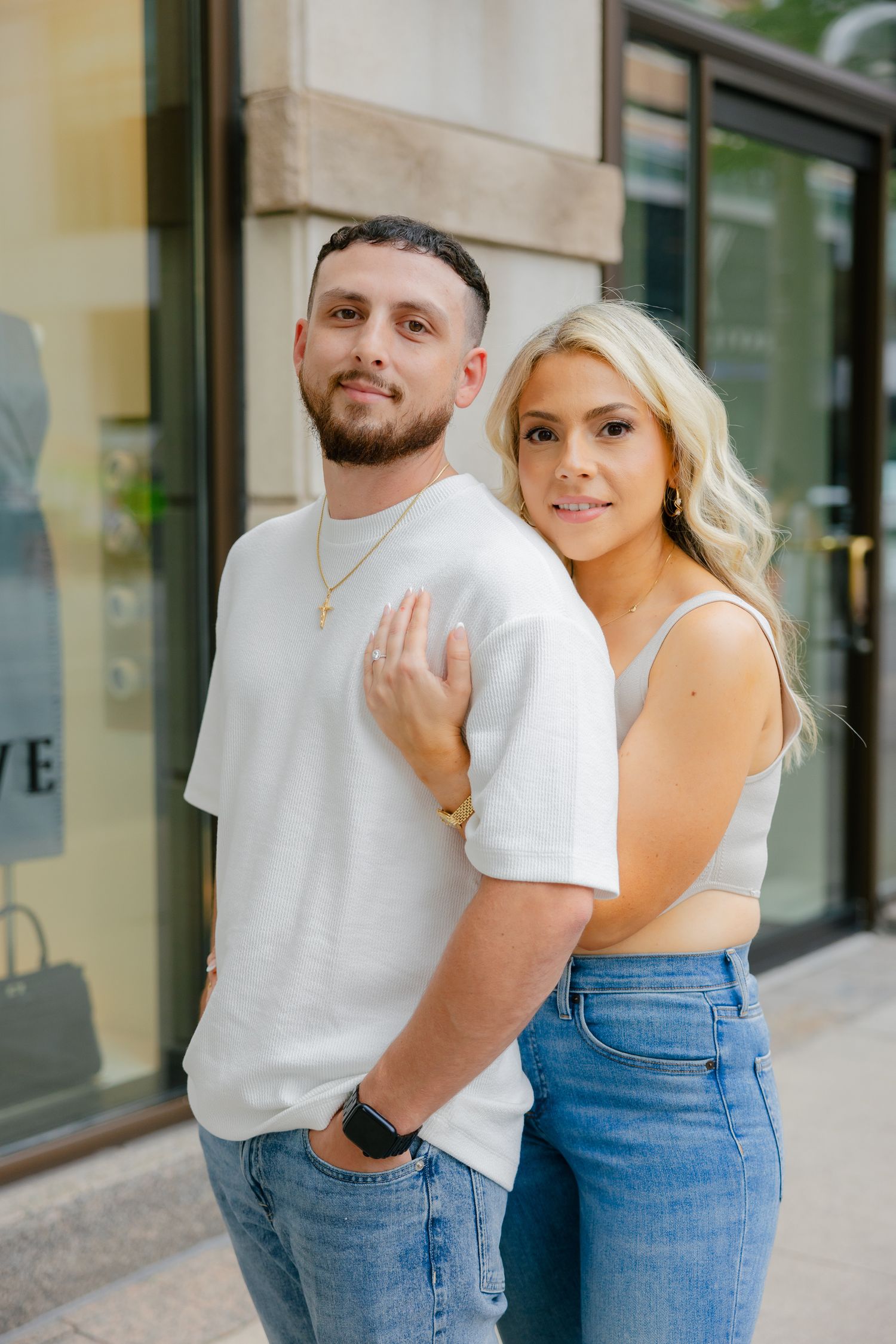 Couple embracing outside store wearing coordinated white and denim outfits.