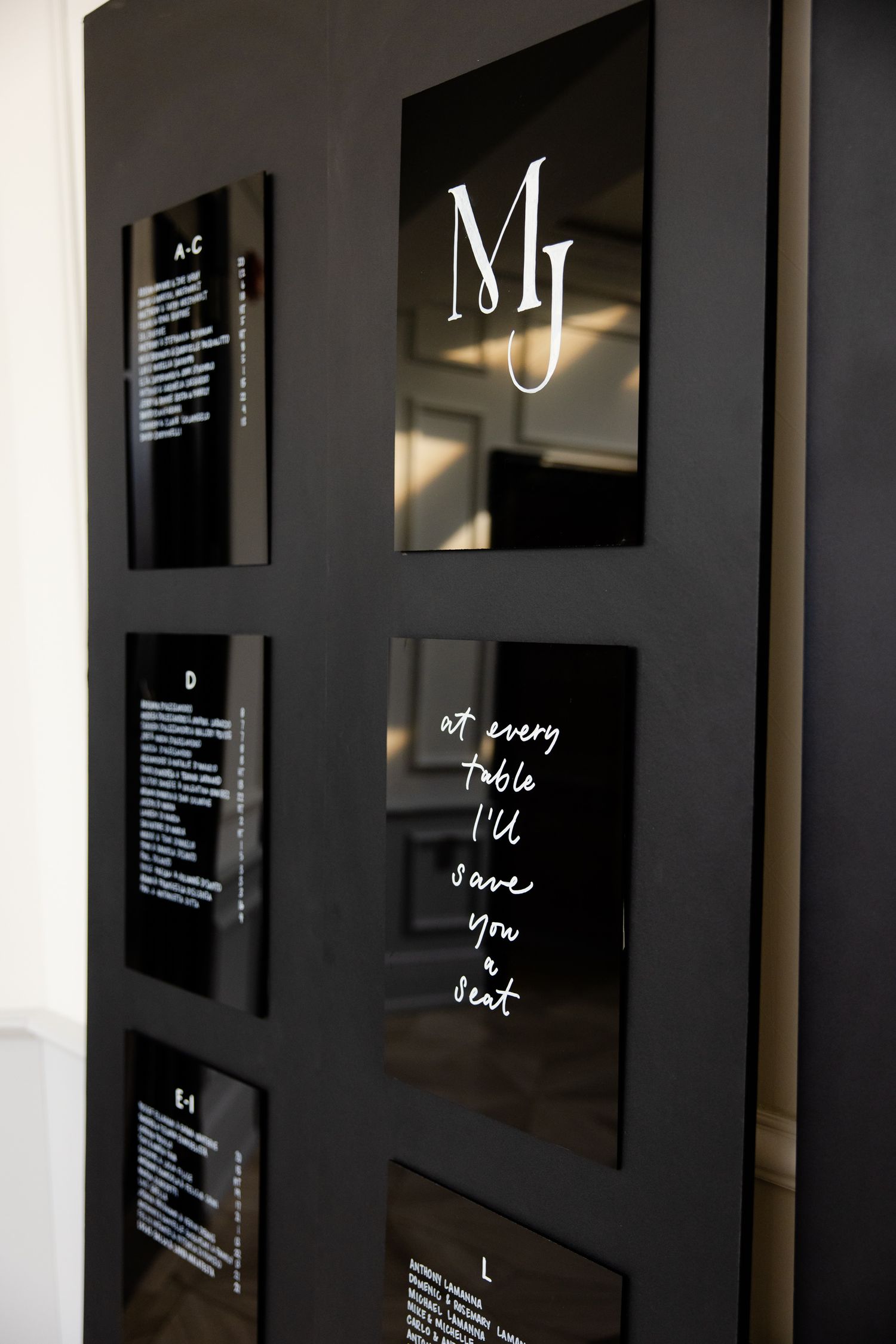 Elegant black wedding signage with monogram and seating assignments in modern white text.