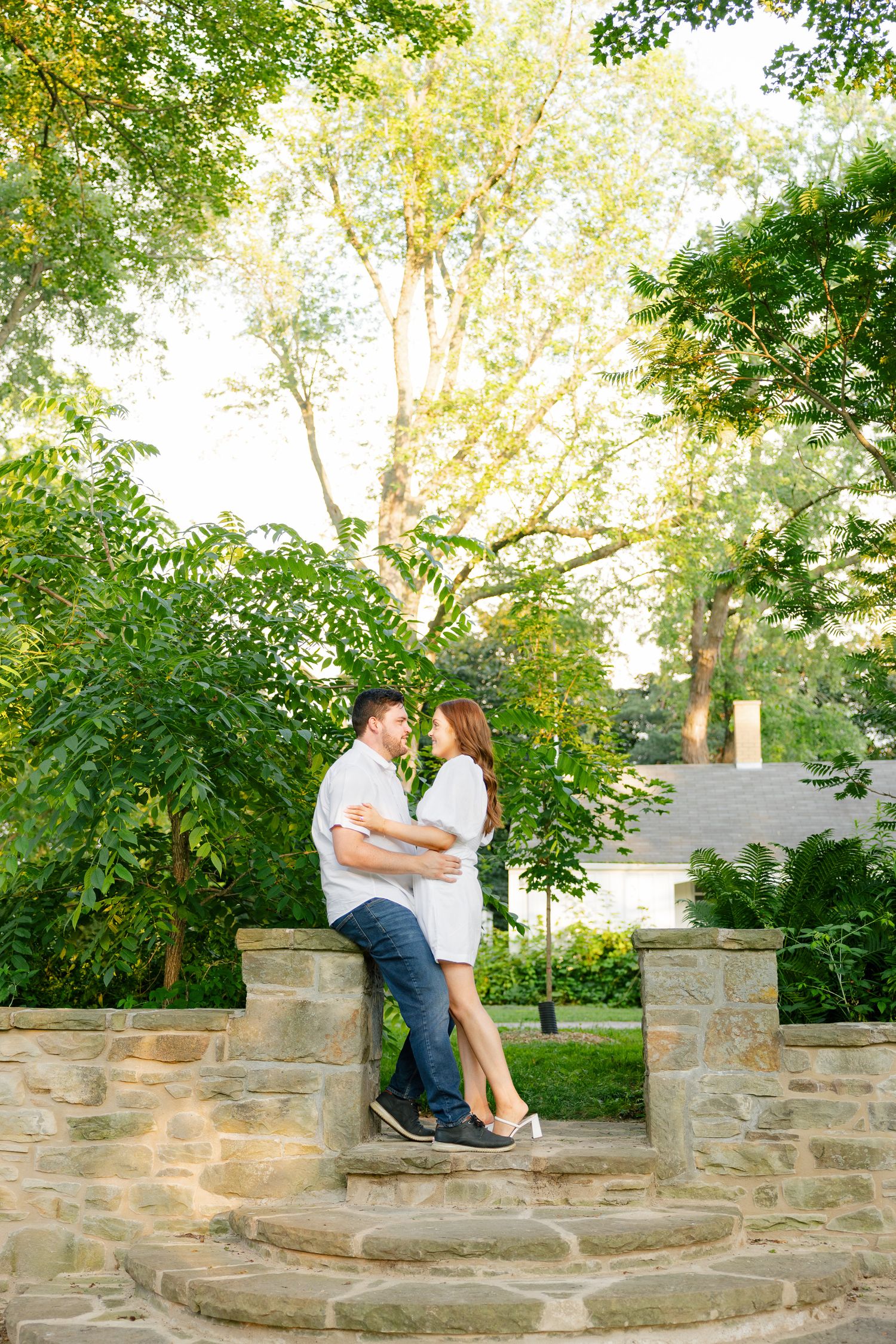 A couple shares a romantic moment on stone garden steps surrounded by lush green foliage at sunset.