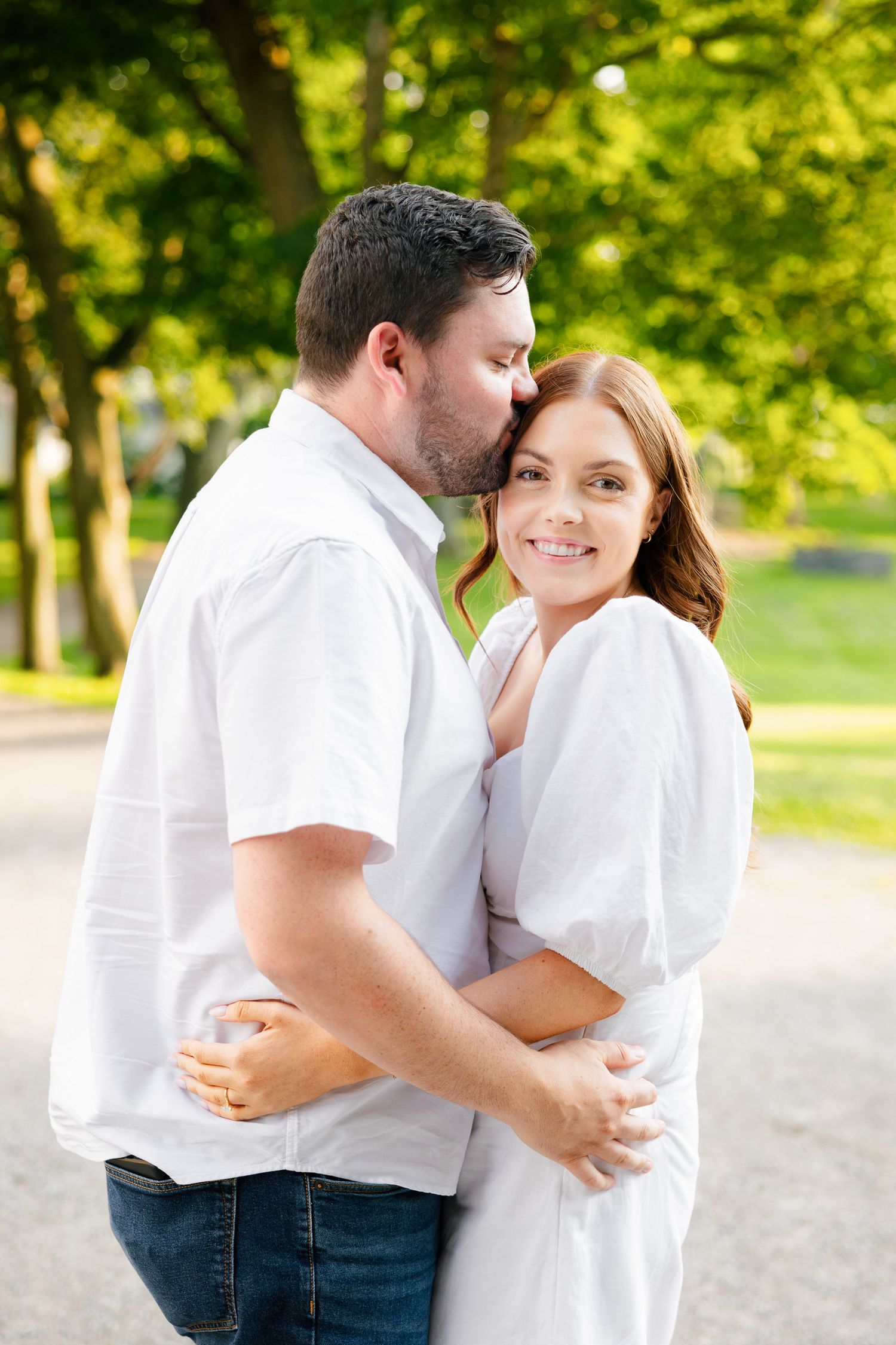 A tender moment between a couple in white clothing against a background of summer trees.