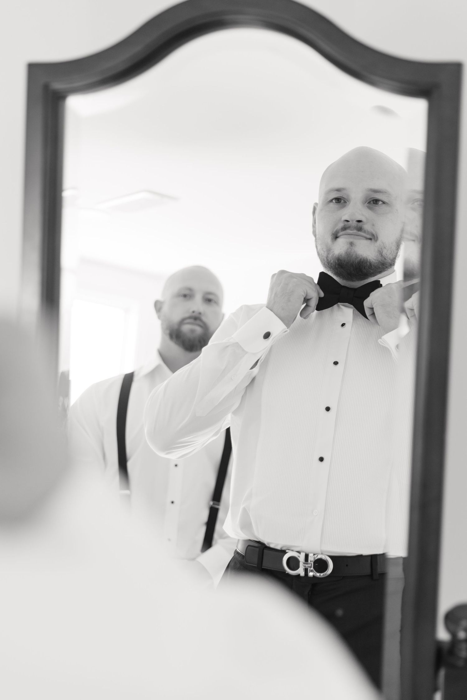 Mirror reflection shows formal attire preparation with bow tie and suspenders.