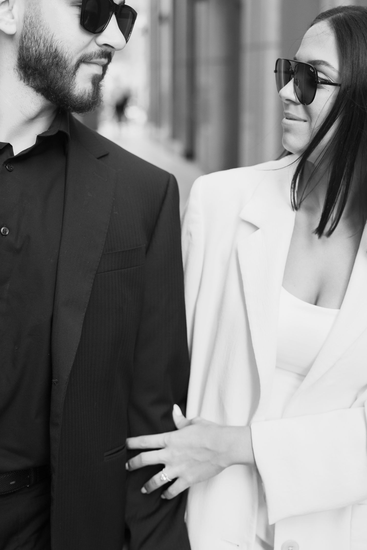 Close-up black and white photo of a couple in sunglasses and contrasting suits.