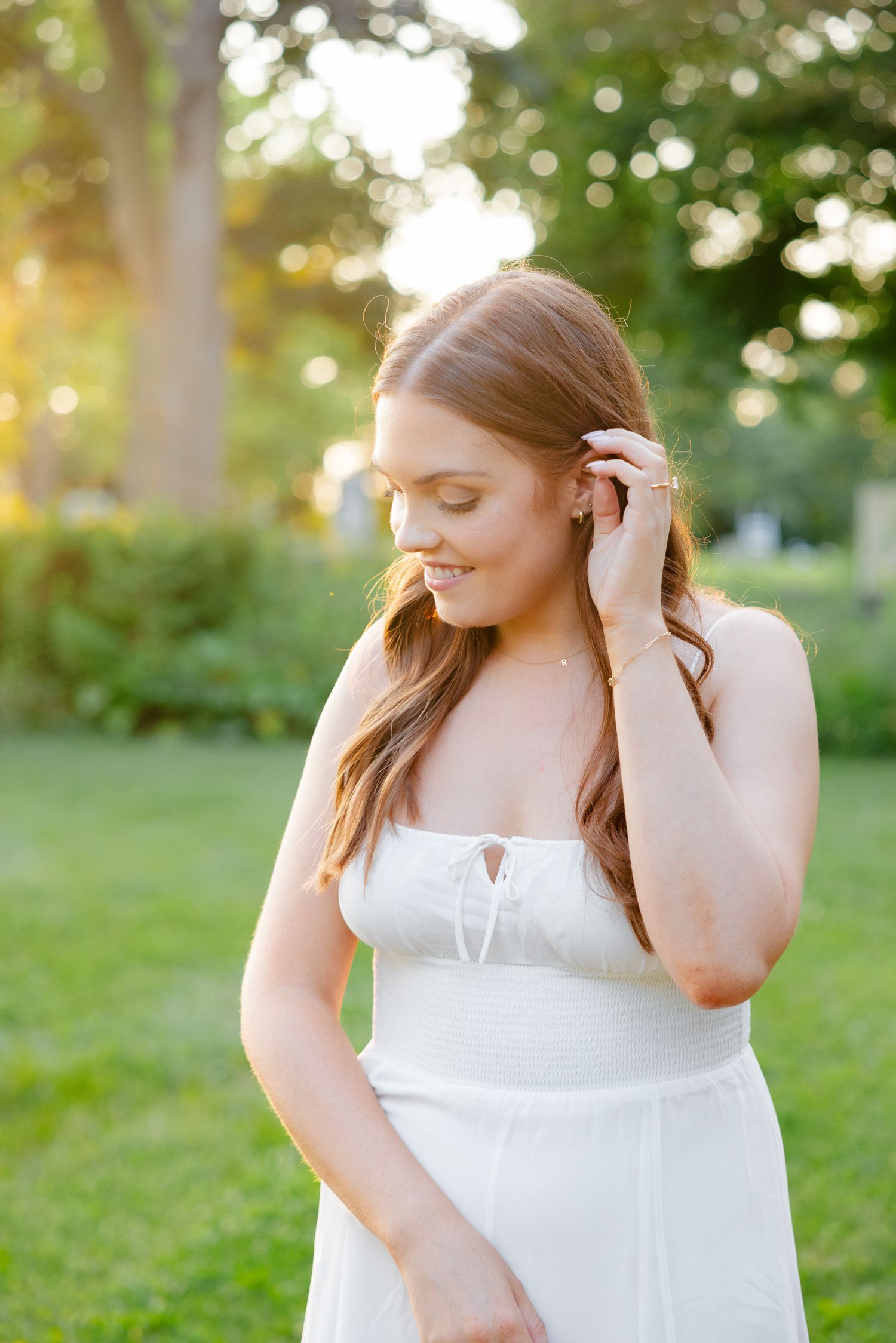 A woman in a white dress poses in a garden setting during golden hour.