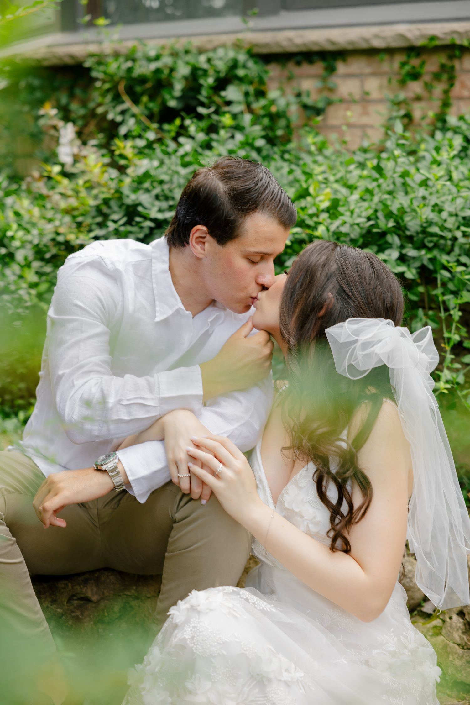 An intimate kiss shared between a couple in a garden setting with natural greenery.