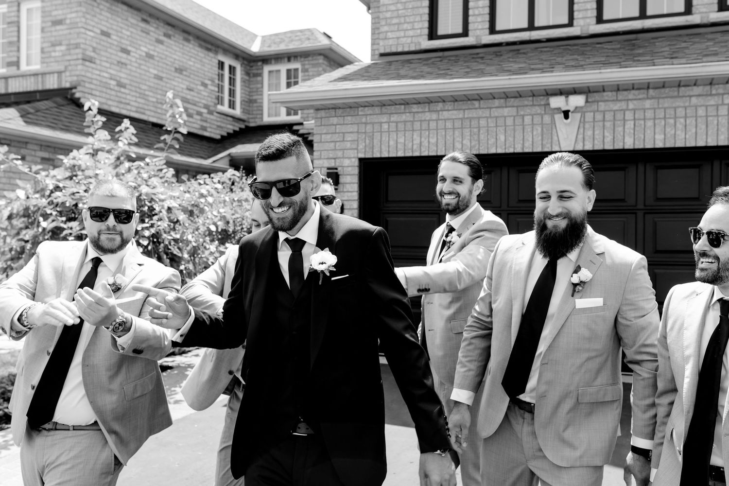 Black and white photo of groomsmen in suits enjoying candid moment outdoors.