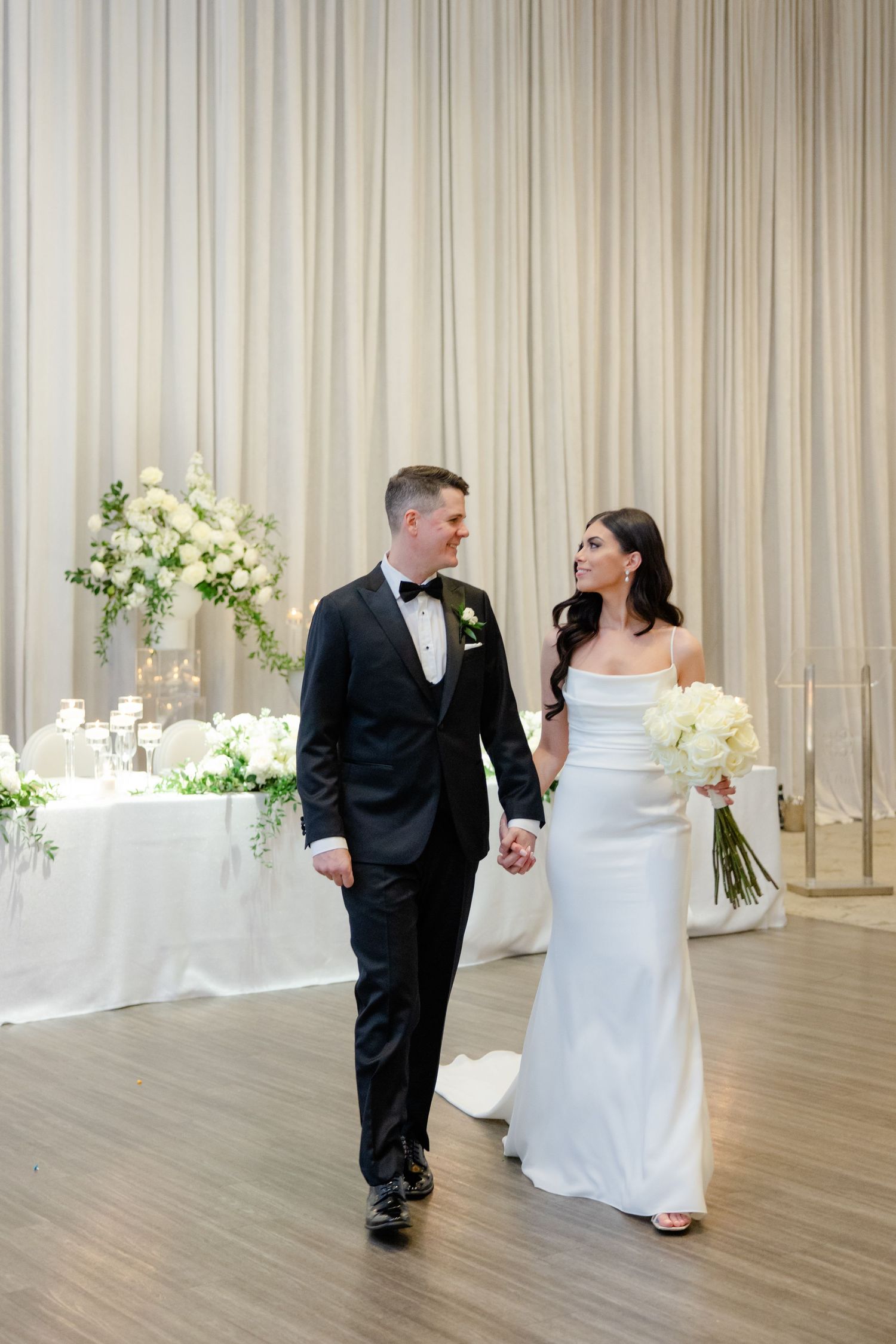 Romantic wedding moment captured in modern reception venue with white drapes and floral decor.