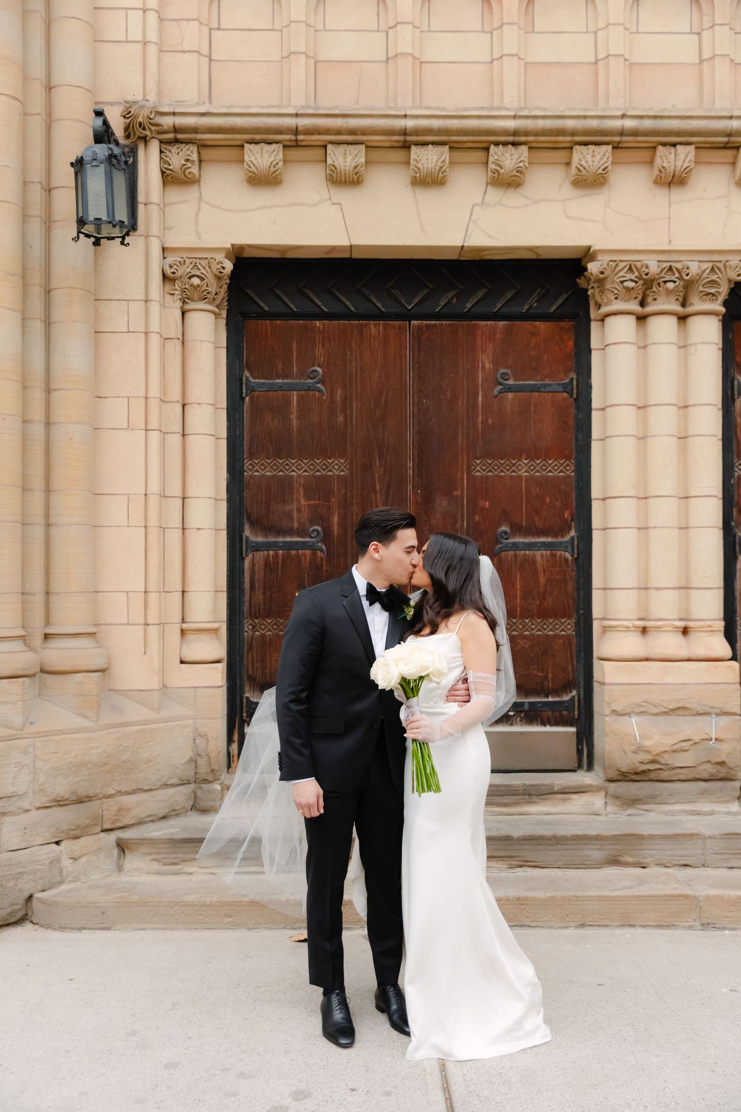 Romantic wedding portrait of couple kissing in front of historic wooden church doors.
