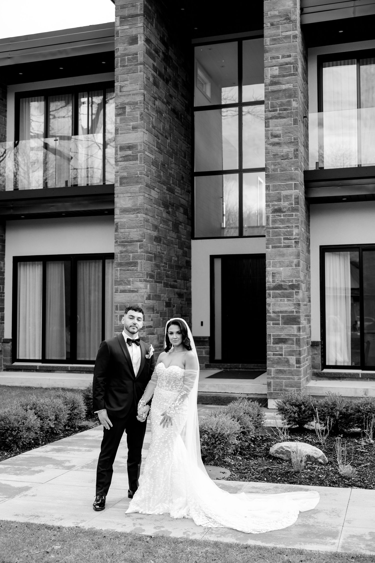 A black and white wedding portrait showcasing a couple in front of contemporary architecture.