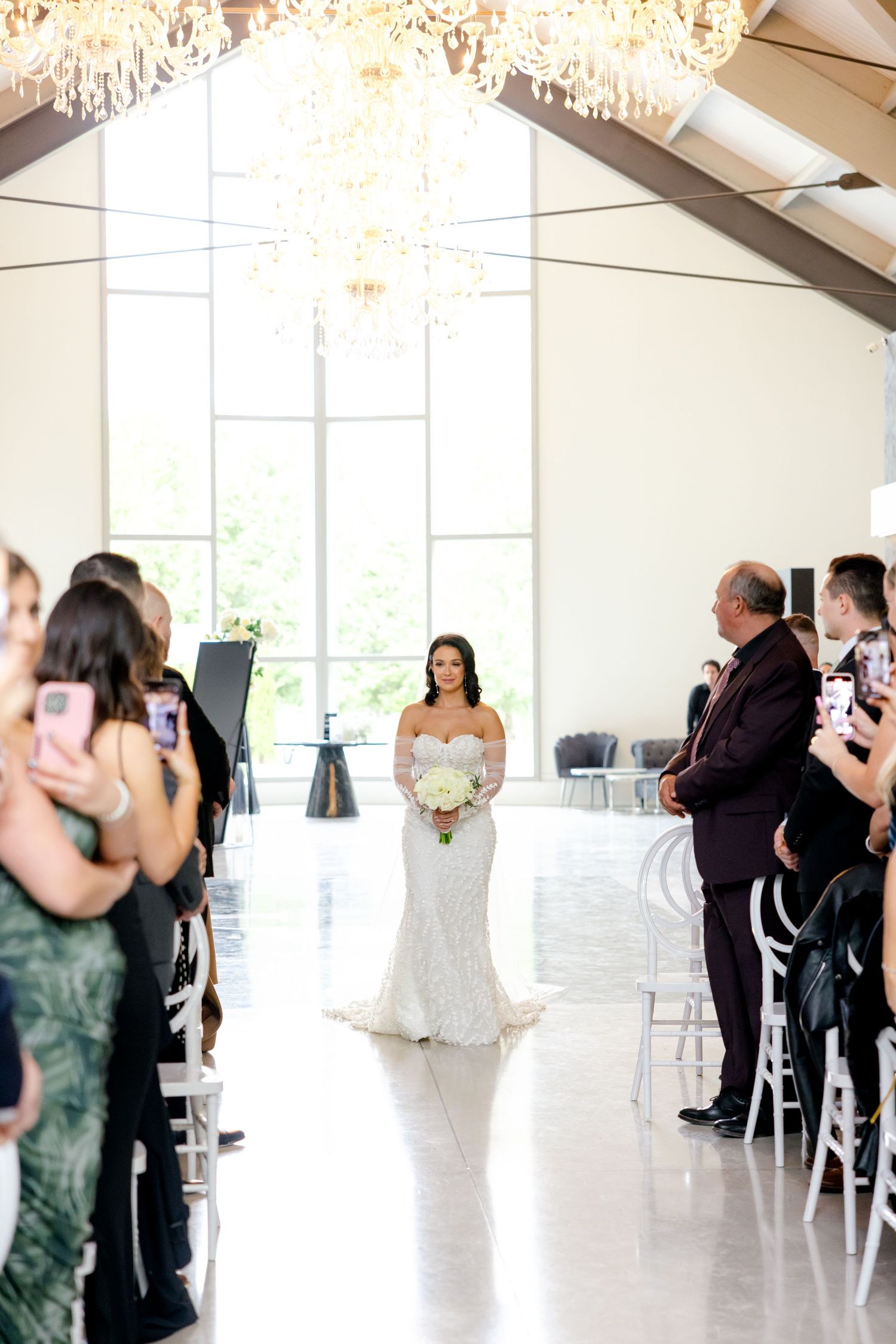 Wedding ceremony in bright modern chapel with crystal chandeliers and white decor.