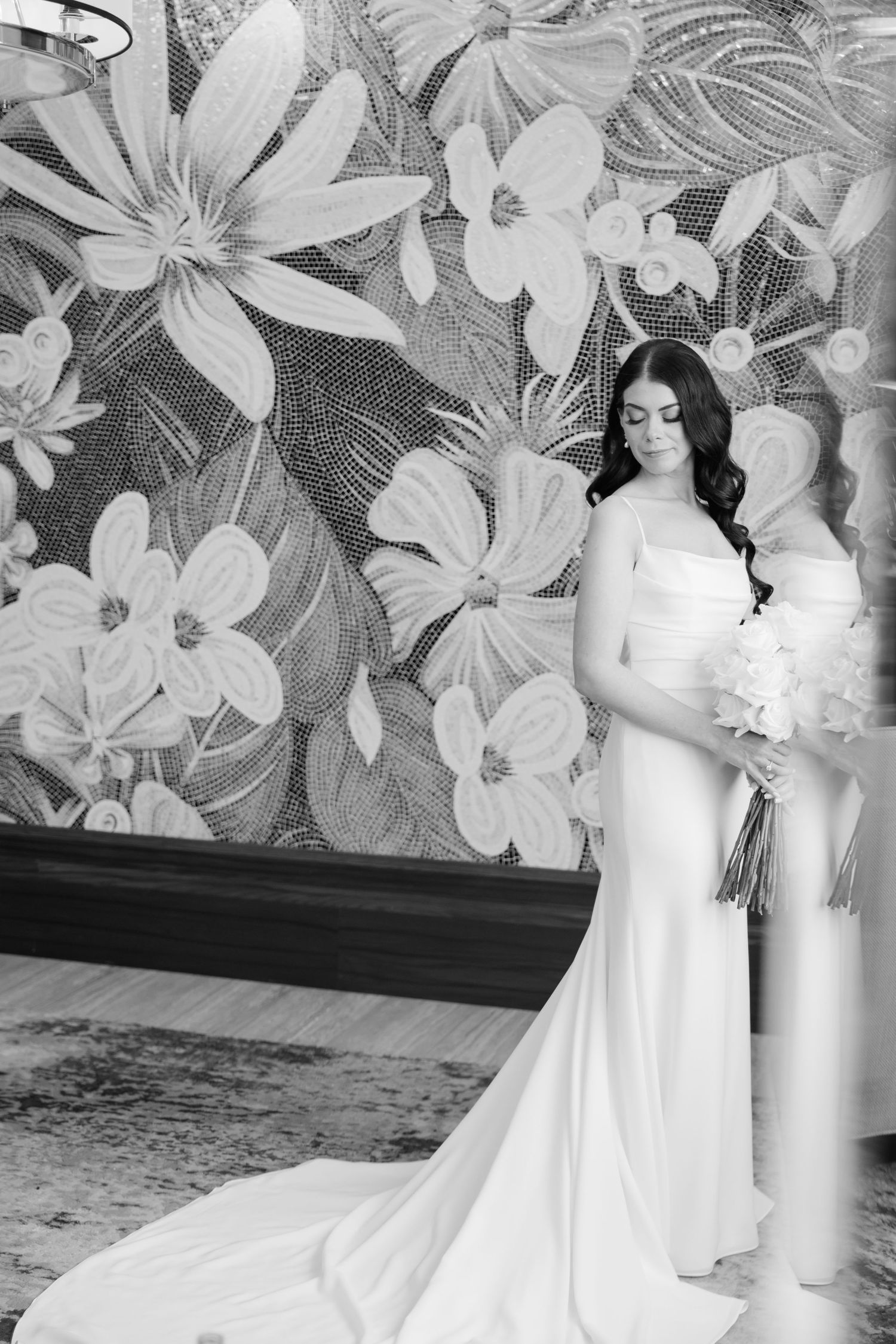 Black and white bridal portrait showcasing a fitted wedding dress against a large floral wall mural.