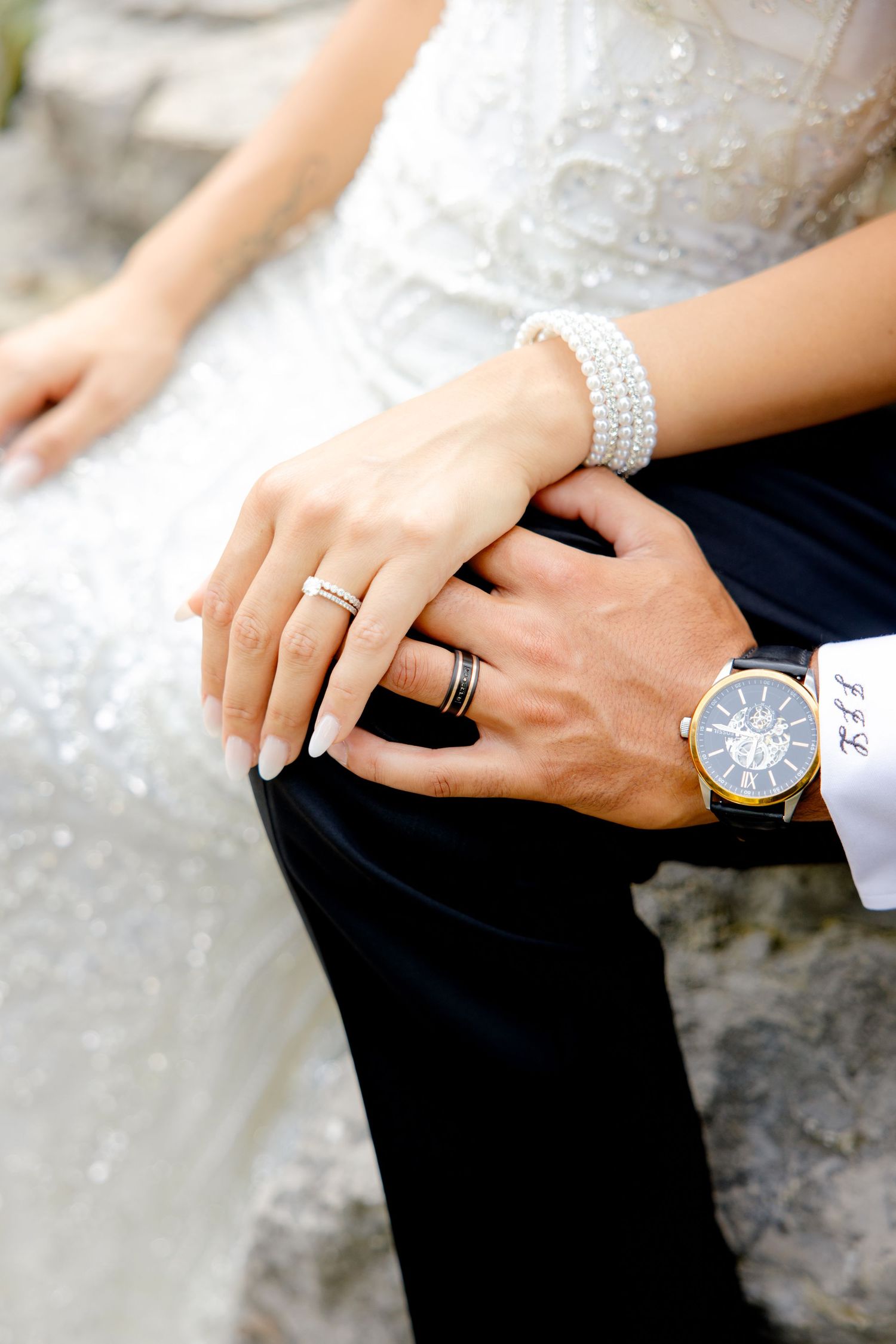 Detail shot of hands with wedding rings, pearl bracelet, and elegant watch.