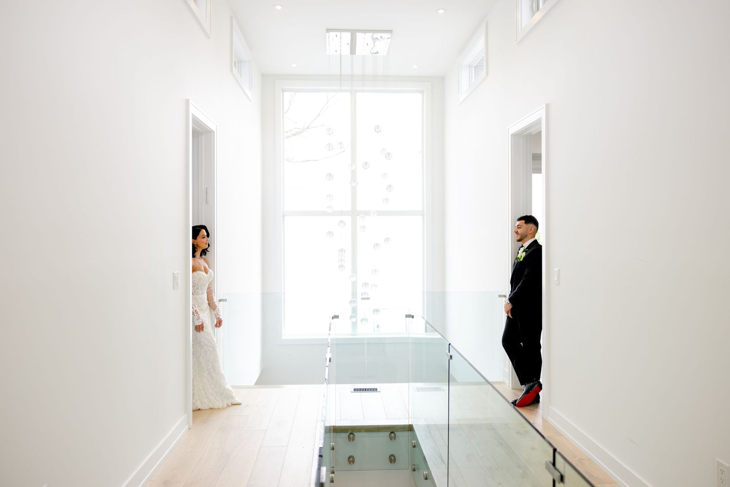 A modern interior hallway featuring white walls and glass railings where two people stand at opposite ends.