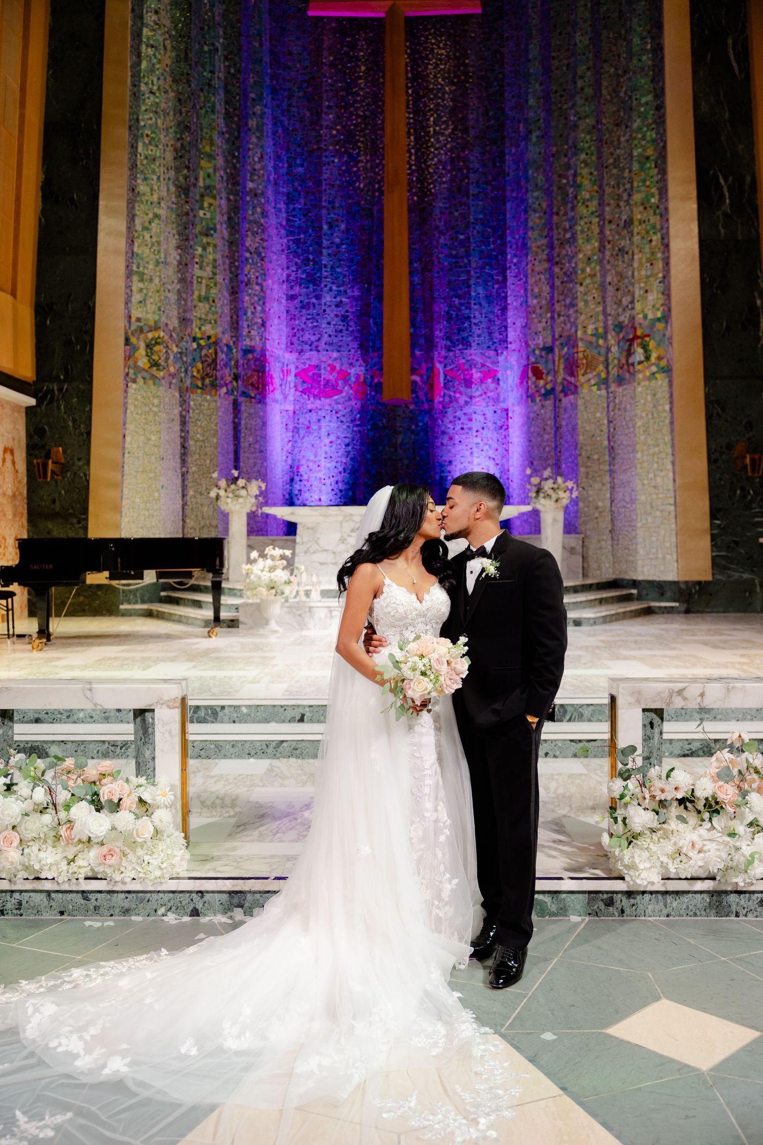 A romantic wedding portrait in a church with purple lighting and a towering cross backdrop.
