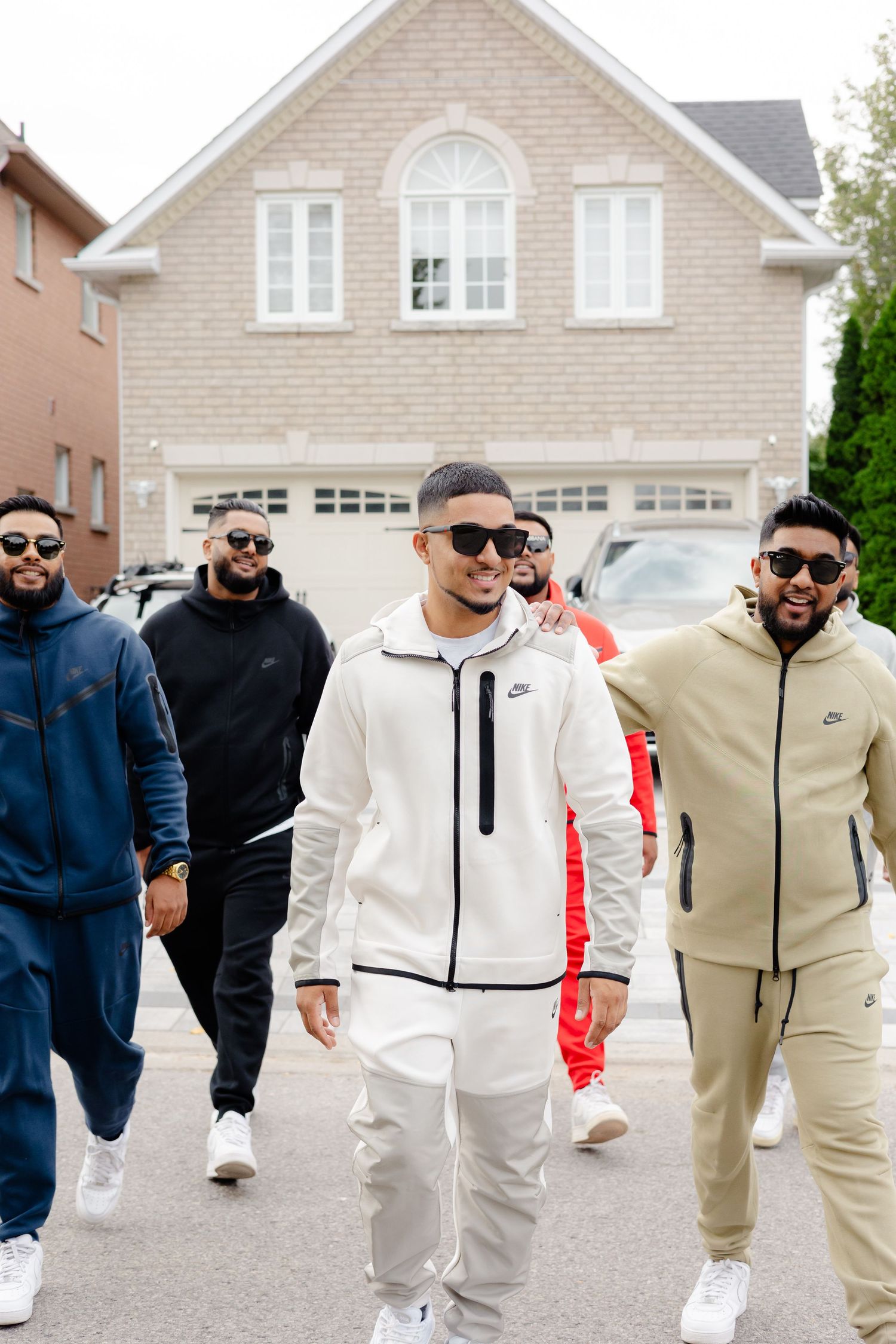 Group wearing trendy athletic wear poses casually in front of a large suburban home.