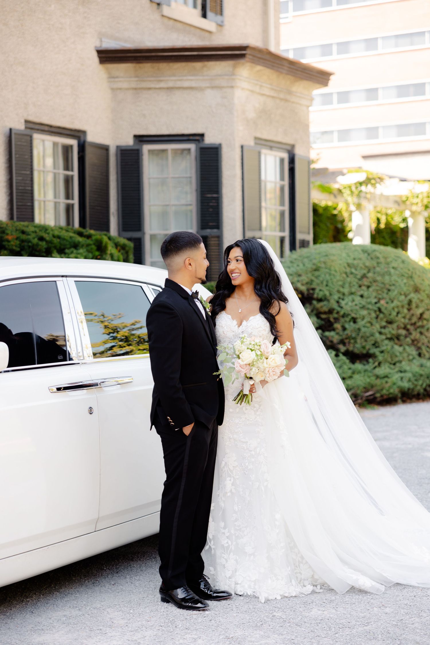 A romantic wedding portrait showing a couple next to a white luxury car at an elegant venue.