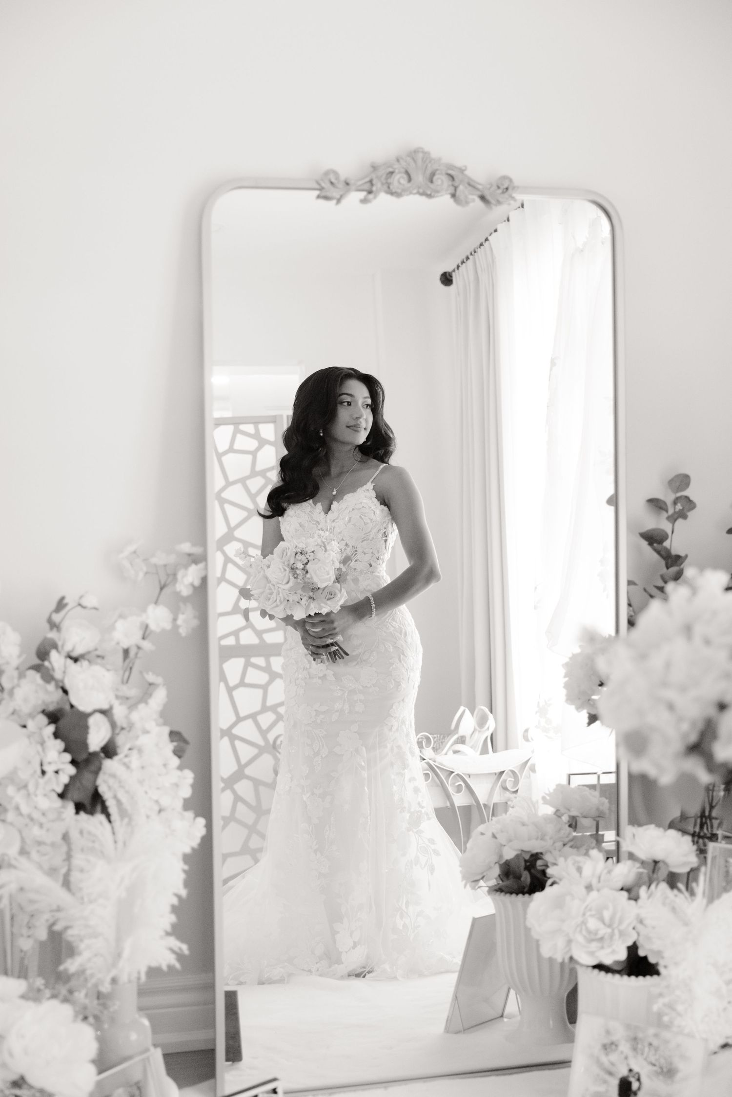 Black and white portrait of wedding gown reflected in vintage mirror with floral decor.