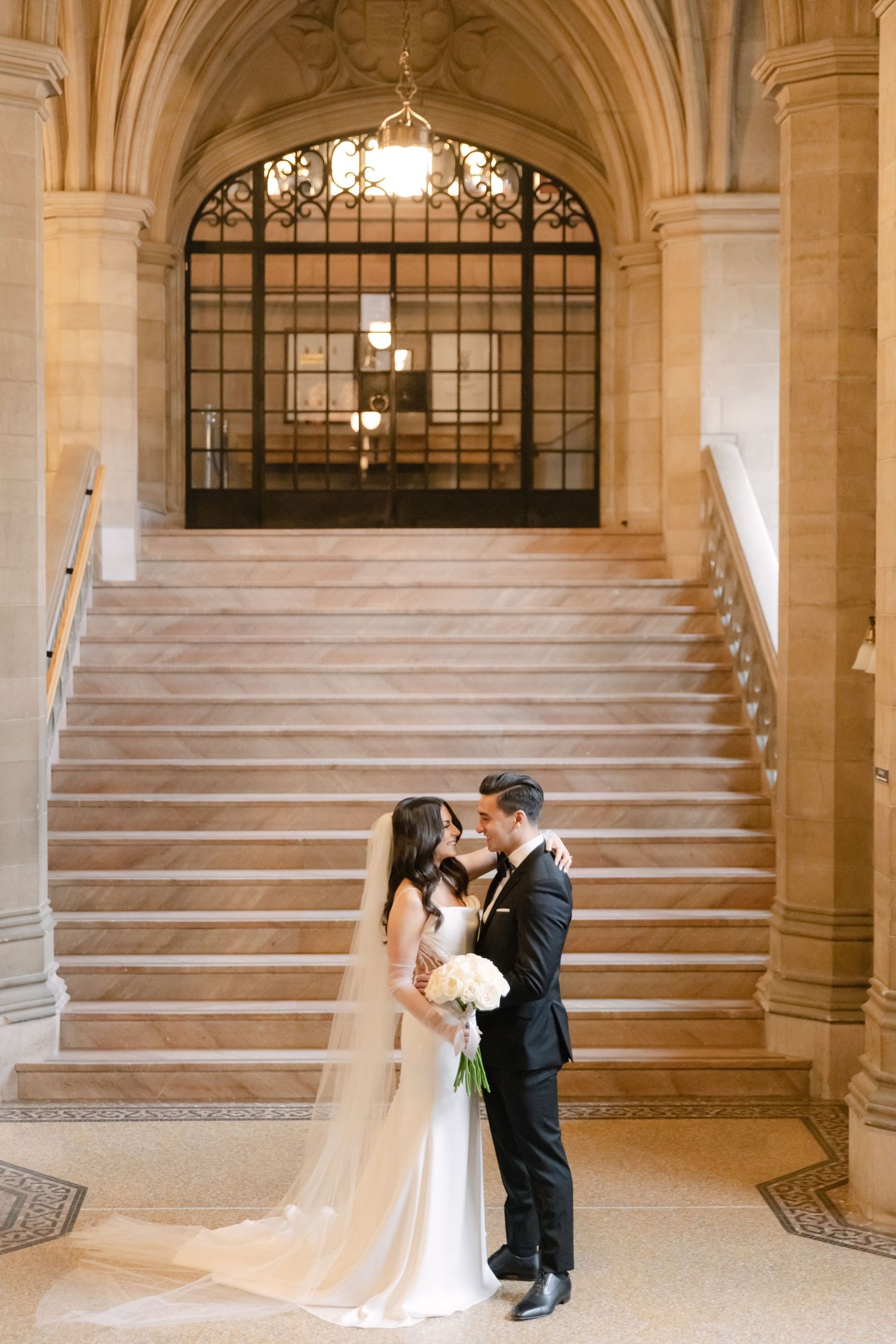 An intimate wedding portrait captured at the bottom of a majestic stone staircase with classic architecture.