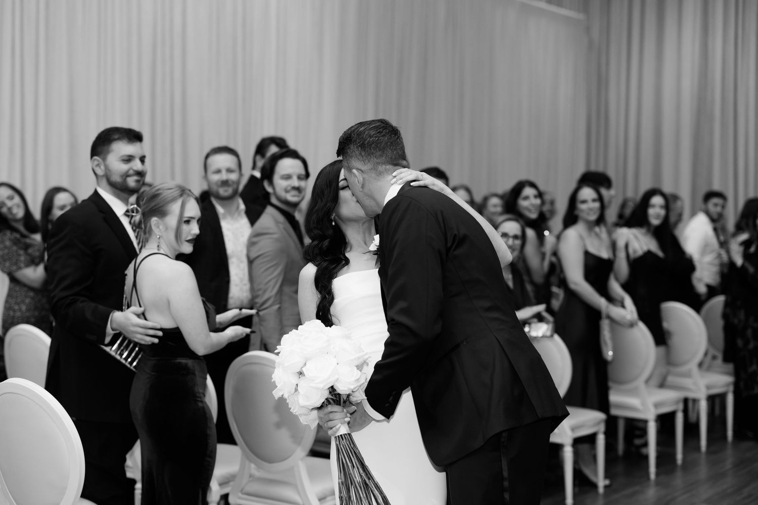 Black and white photo of a couple sharing a joyful moment during their first dance at a wedding reception.
