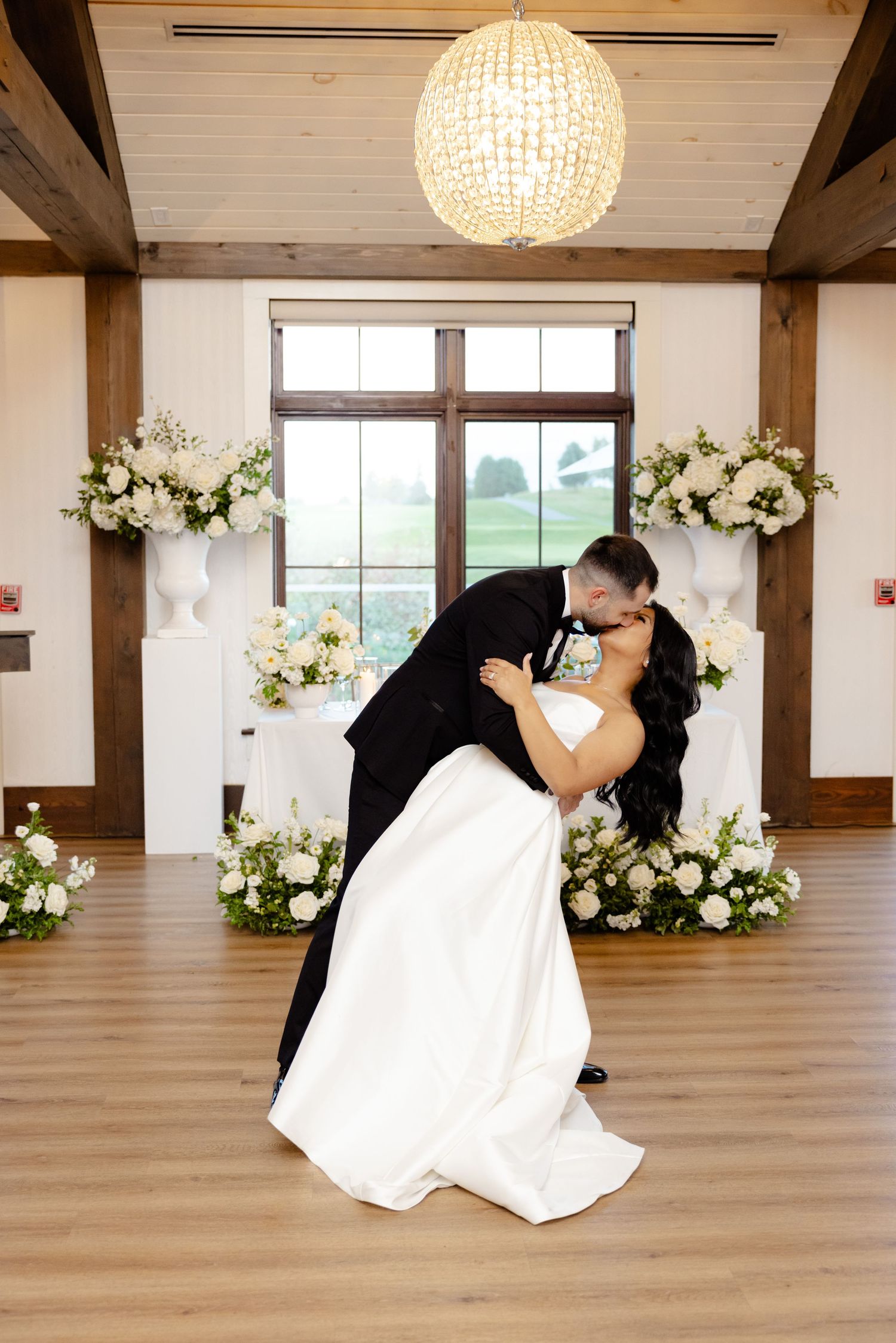 A romantic dip during a wedding dance surrounded by elegant white floral arrangements.