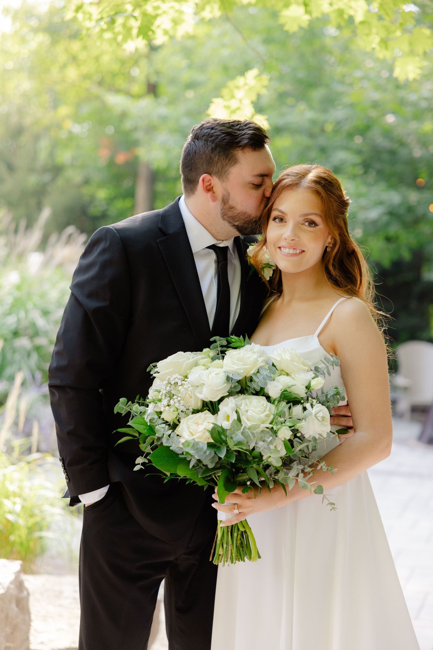 A romantic wedding portrait featuring a couple with a luxurious white bouquet in a garden setting.