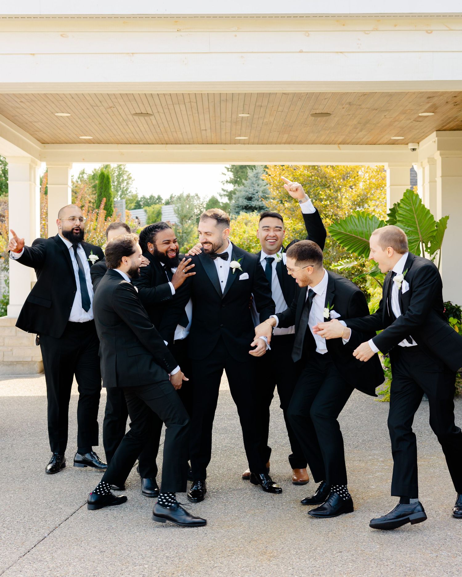 Wedding party members in black suits acting silly and energetic during photo session.