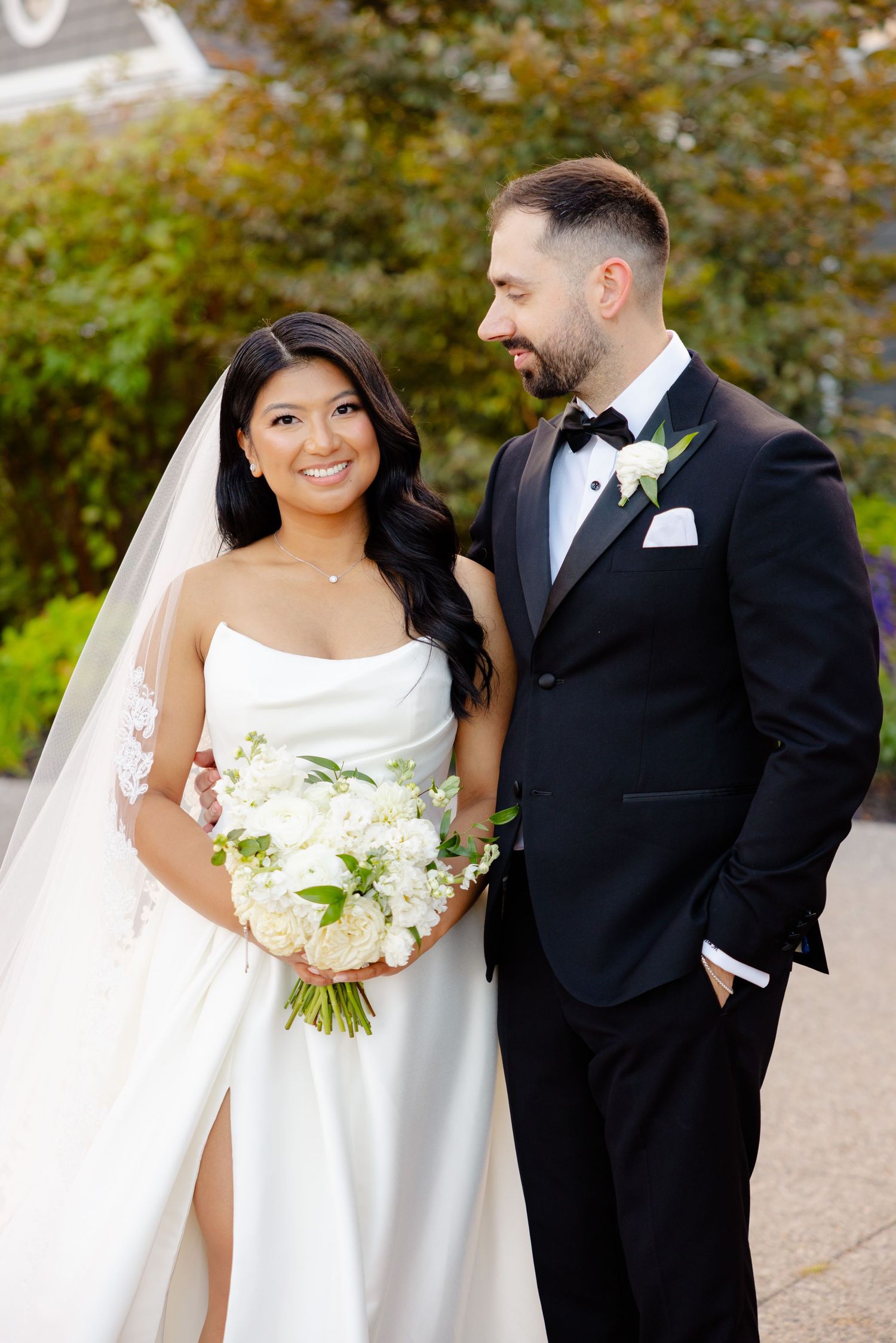 A joyful wedding couple shares a candid moment in front of landscaped gardens.