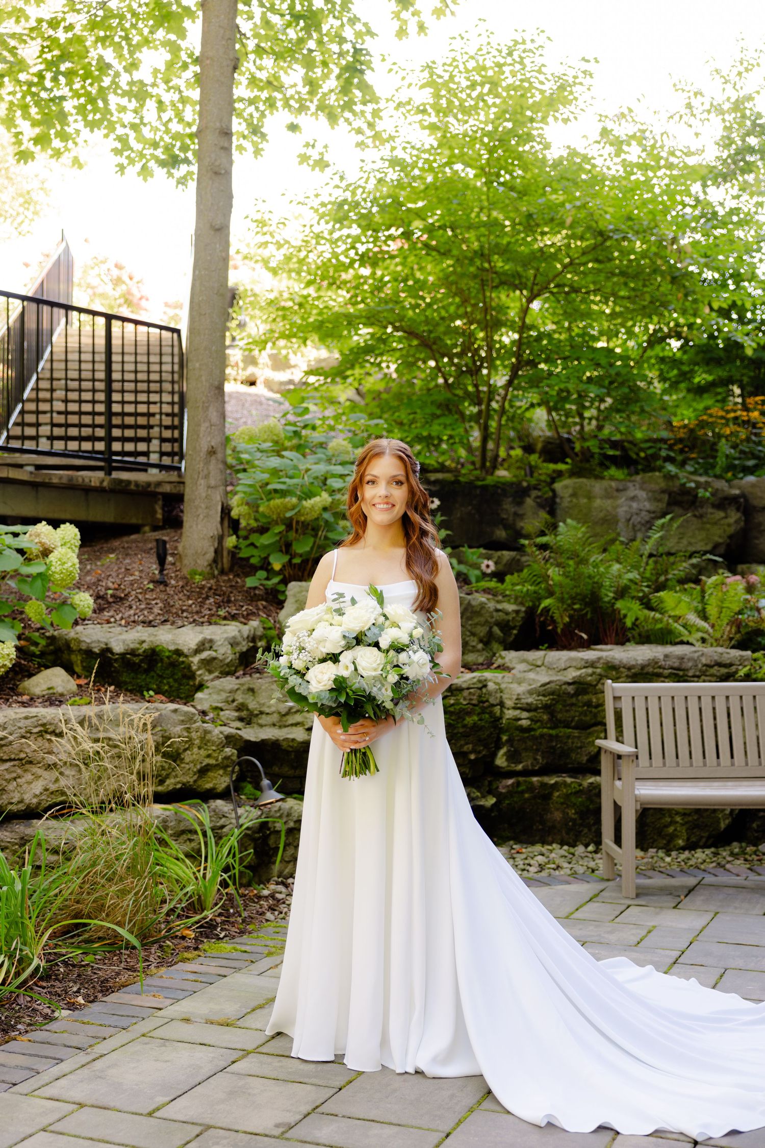 Elegant bridal portrait in a garden setting with stone steps and lush greenery.