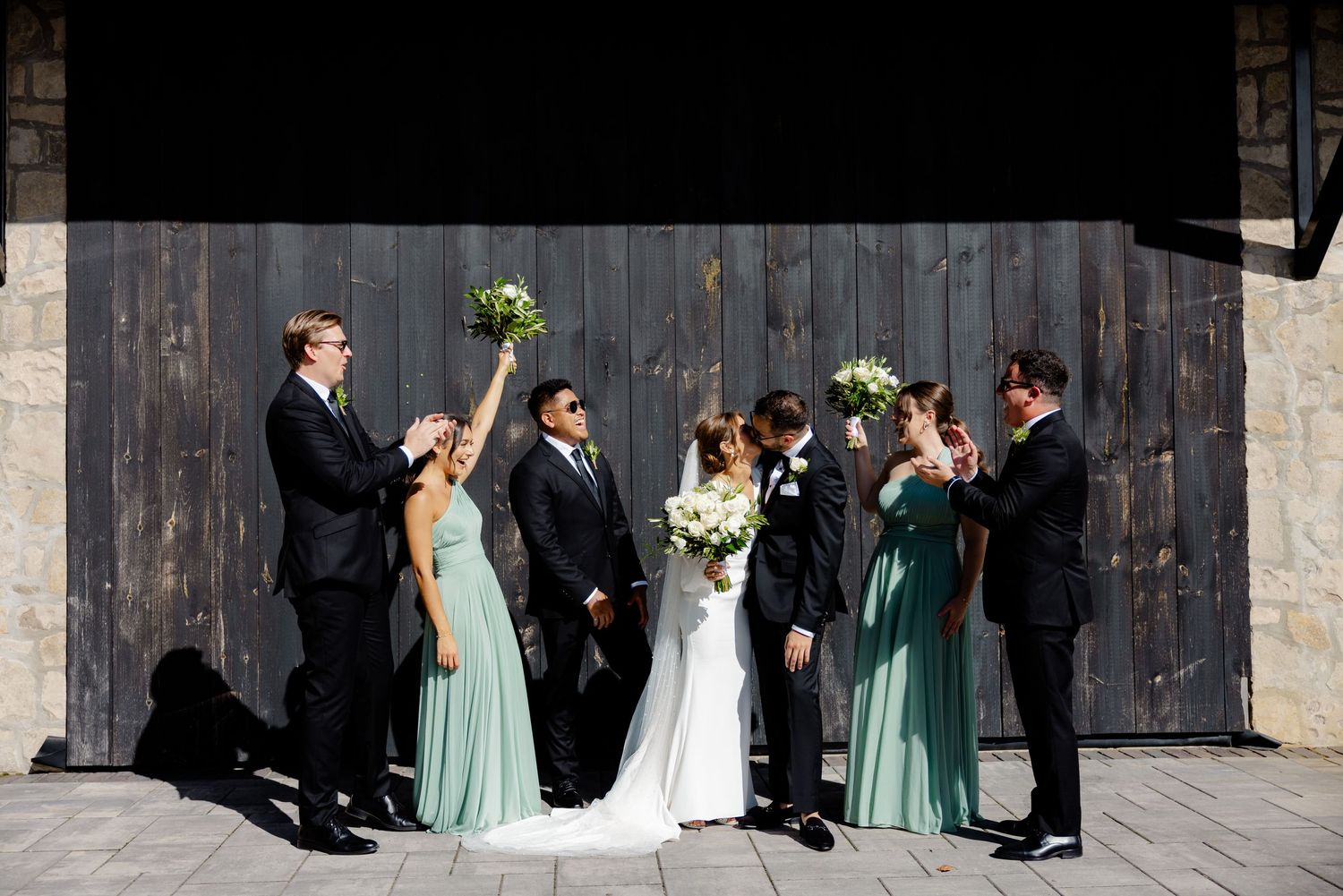 Wedding party laughing and celebrating in front of a rustic barn door background.