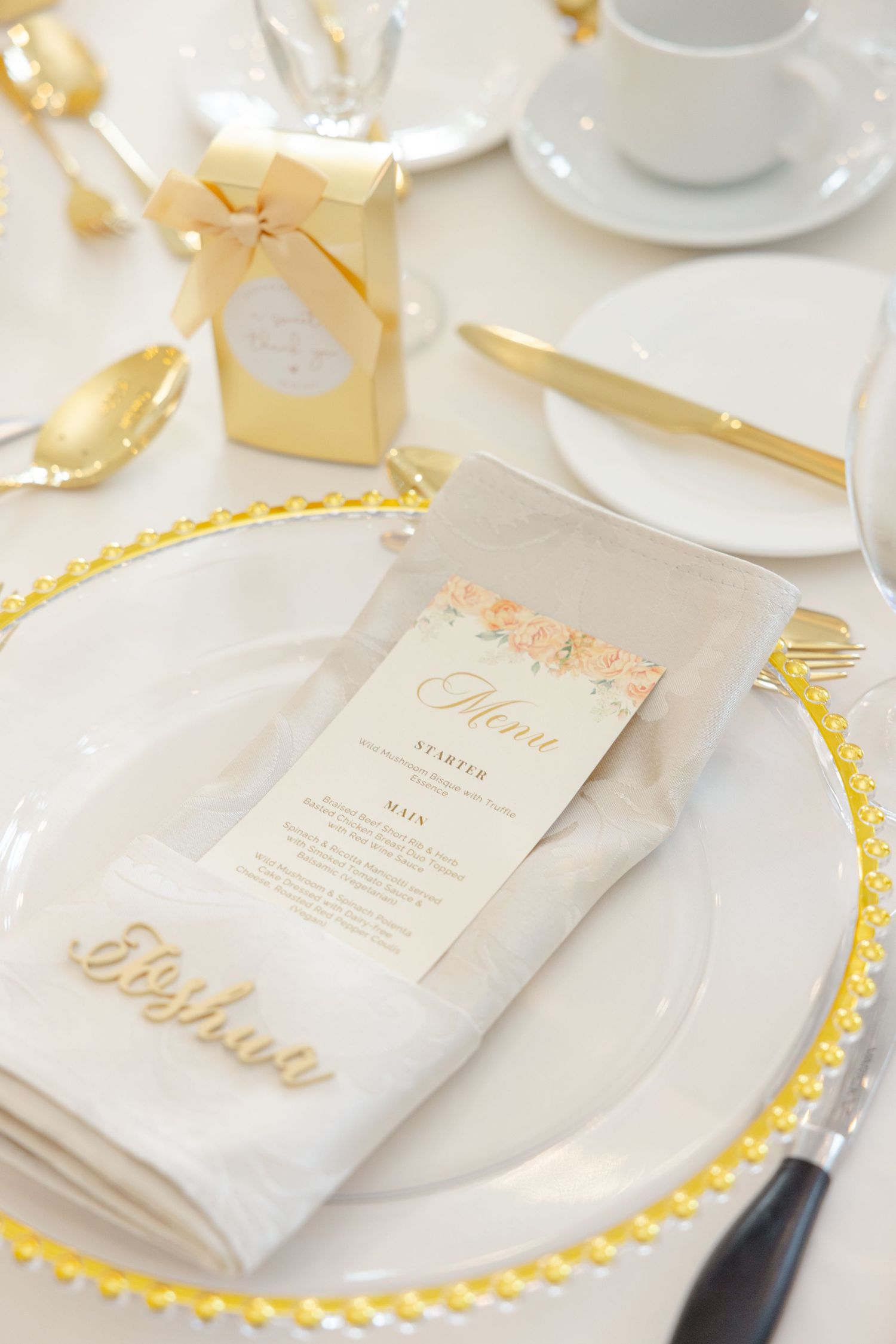 Gold and white place setting with menu card and charger plate at wedding reception.