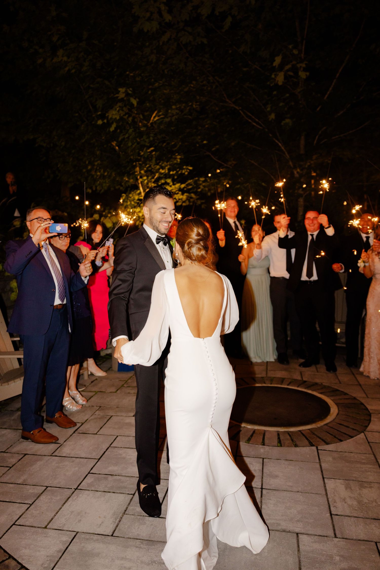 A back view of a bride in a backless white gown dancing with her groom at the reception.