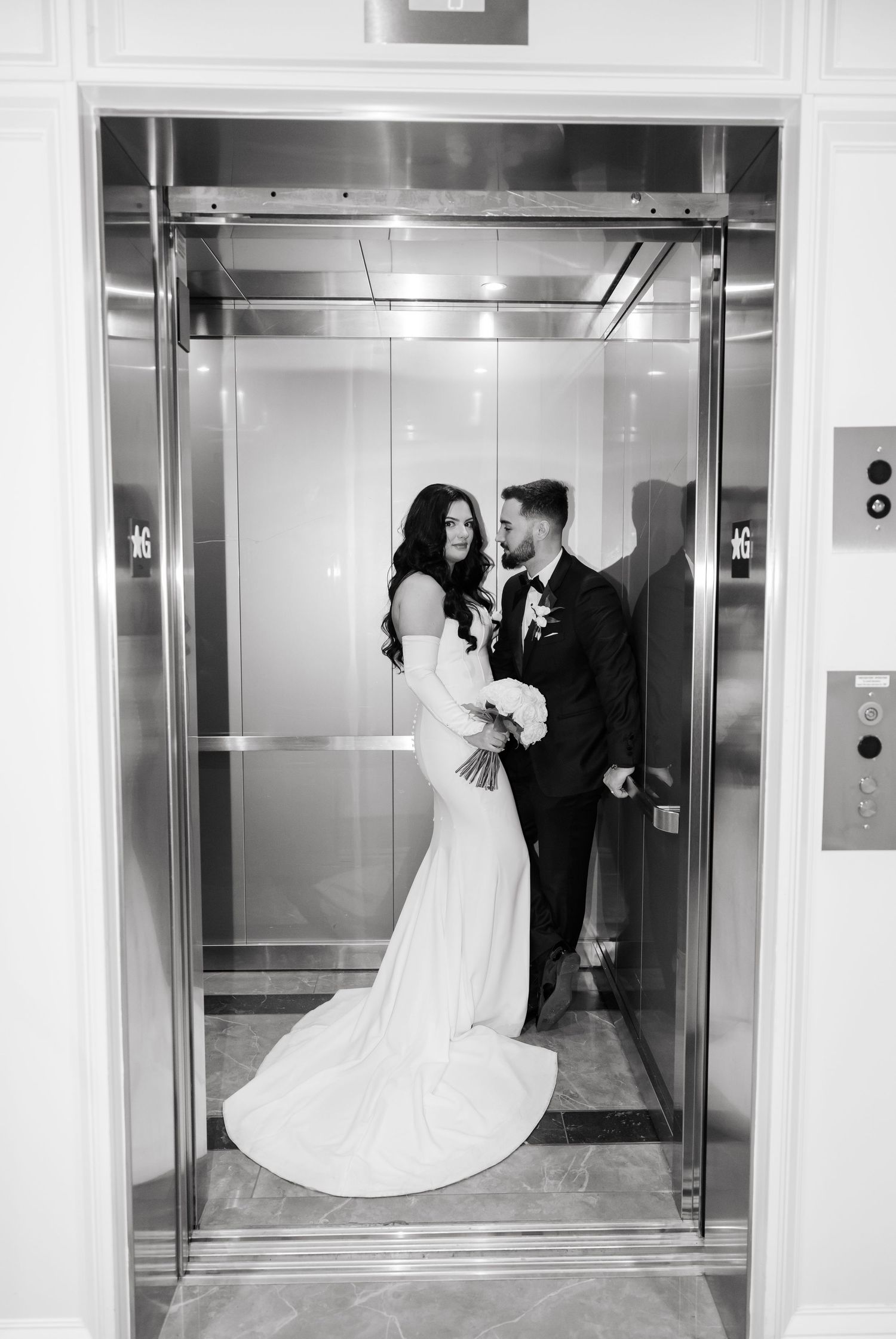 Romantic black and white elevator photo of newlyweds in formal wedding attire.