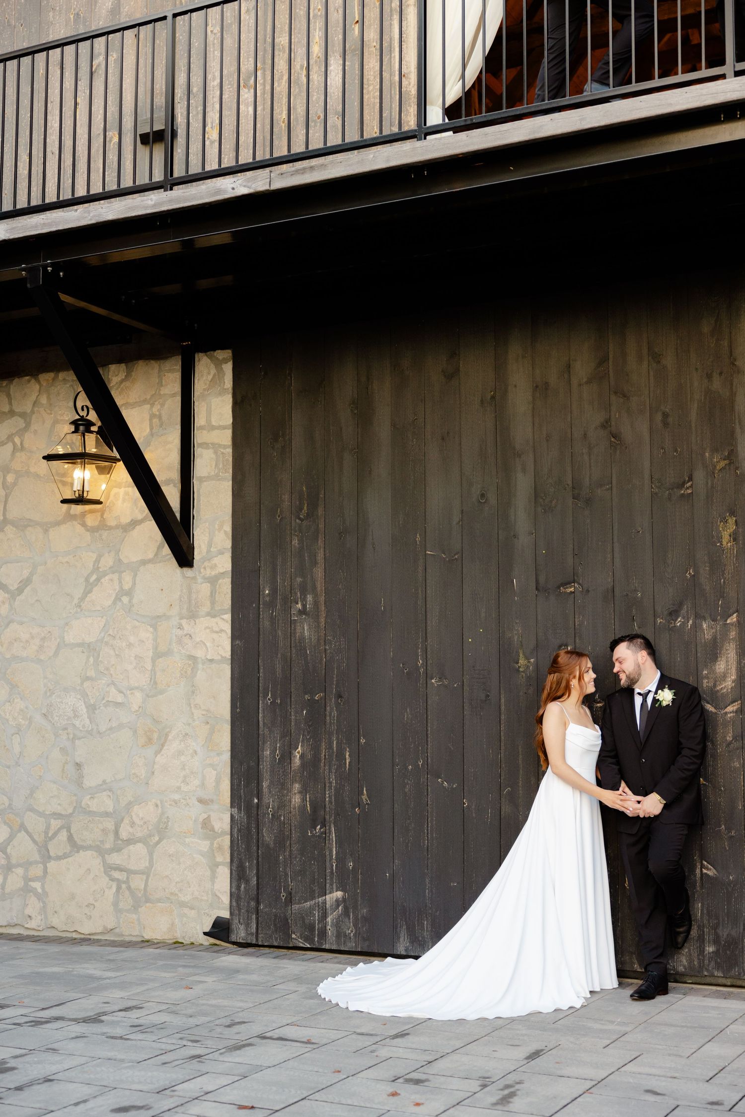 Wedding couple poses beneath balcony against stone and wood wall with lantern.
