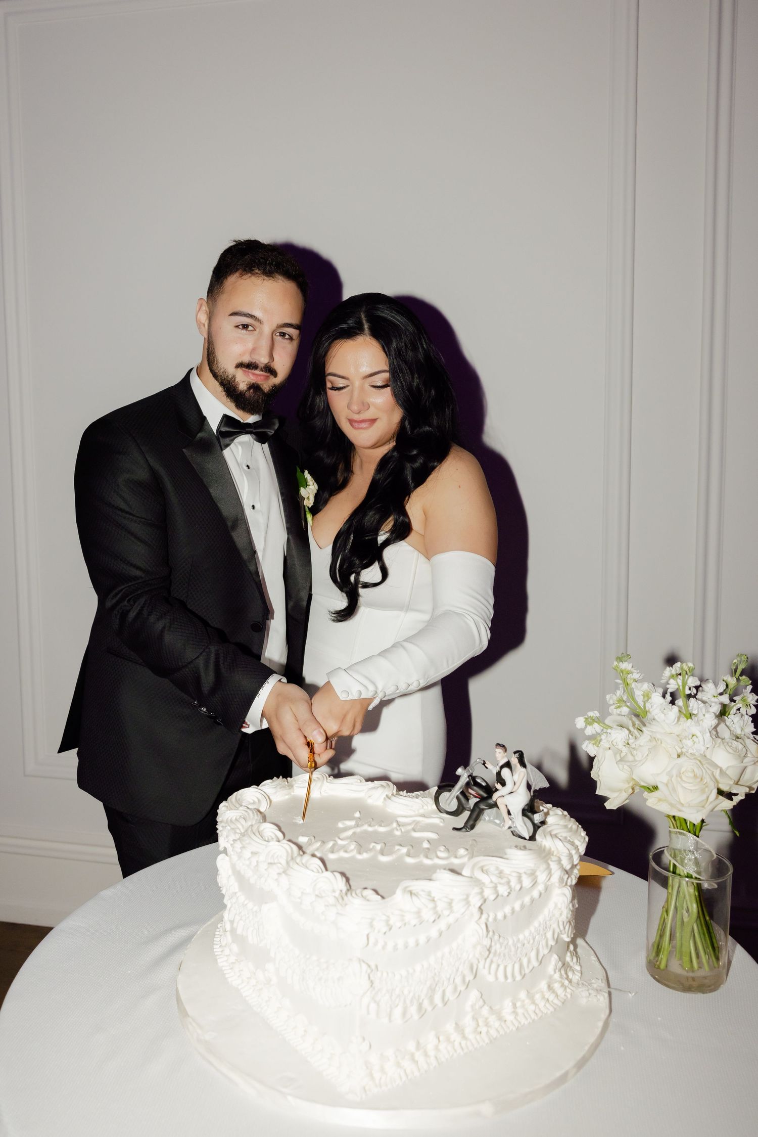 Newlyweds cut their white wedding cake together at an elegant reception.
