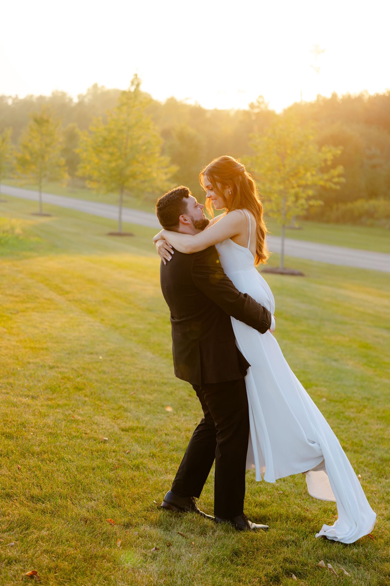Wedding couple dances and embraces on a grassy hill during golden hour photography session.
