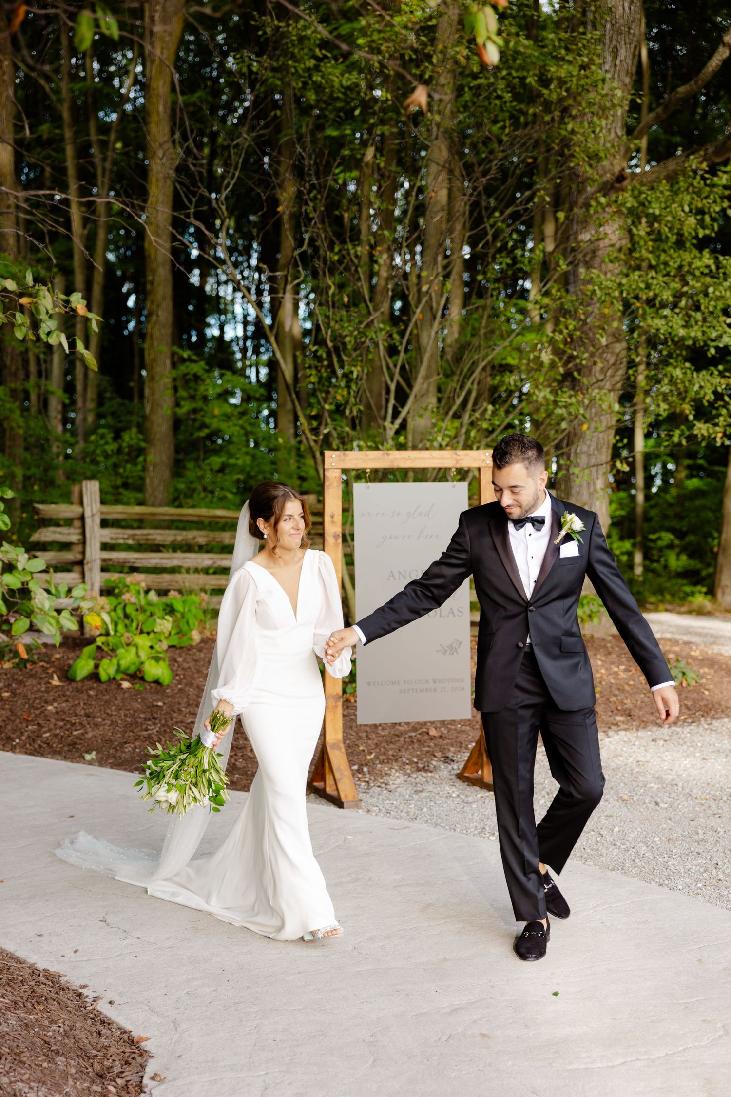 Couple shares a playful moment while walking along a winding forest path near a framed sign.