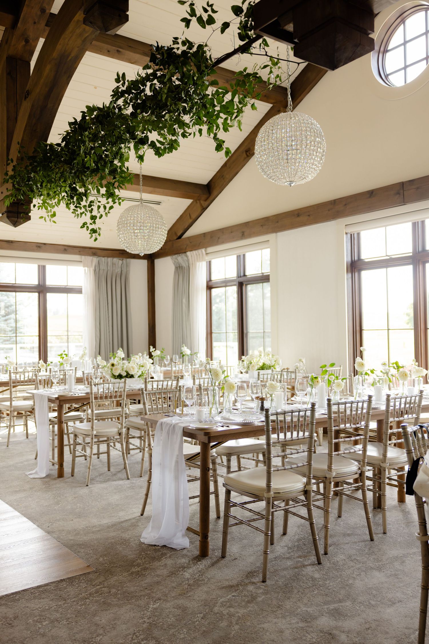 Rustic wedding venue with vaulted wood beam ceiling, crystal chandeliers, and greenery decorations.