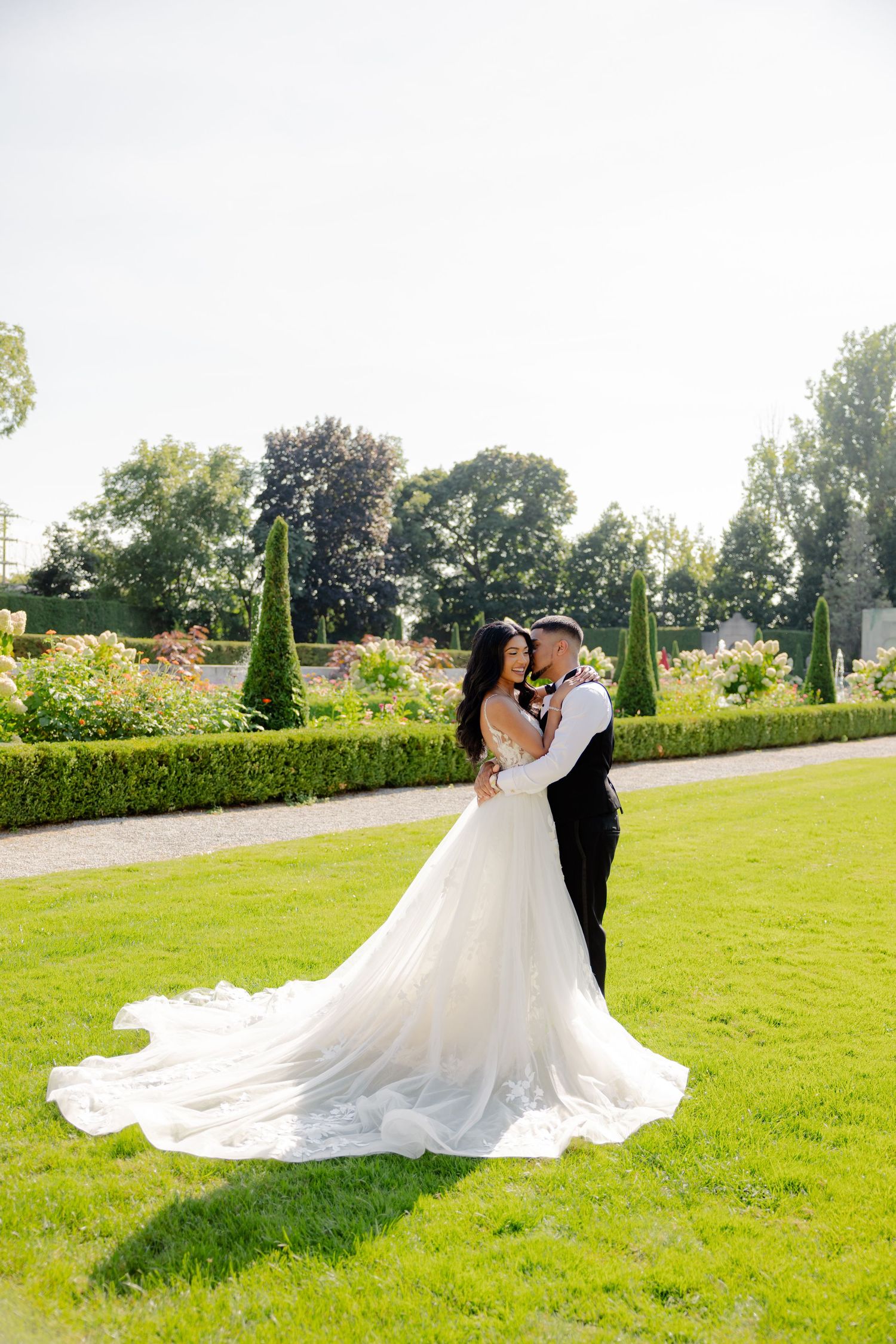 Elegant wedding photograph capturing a couple's embrace against a backdrop of formal gardens.