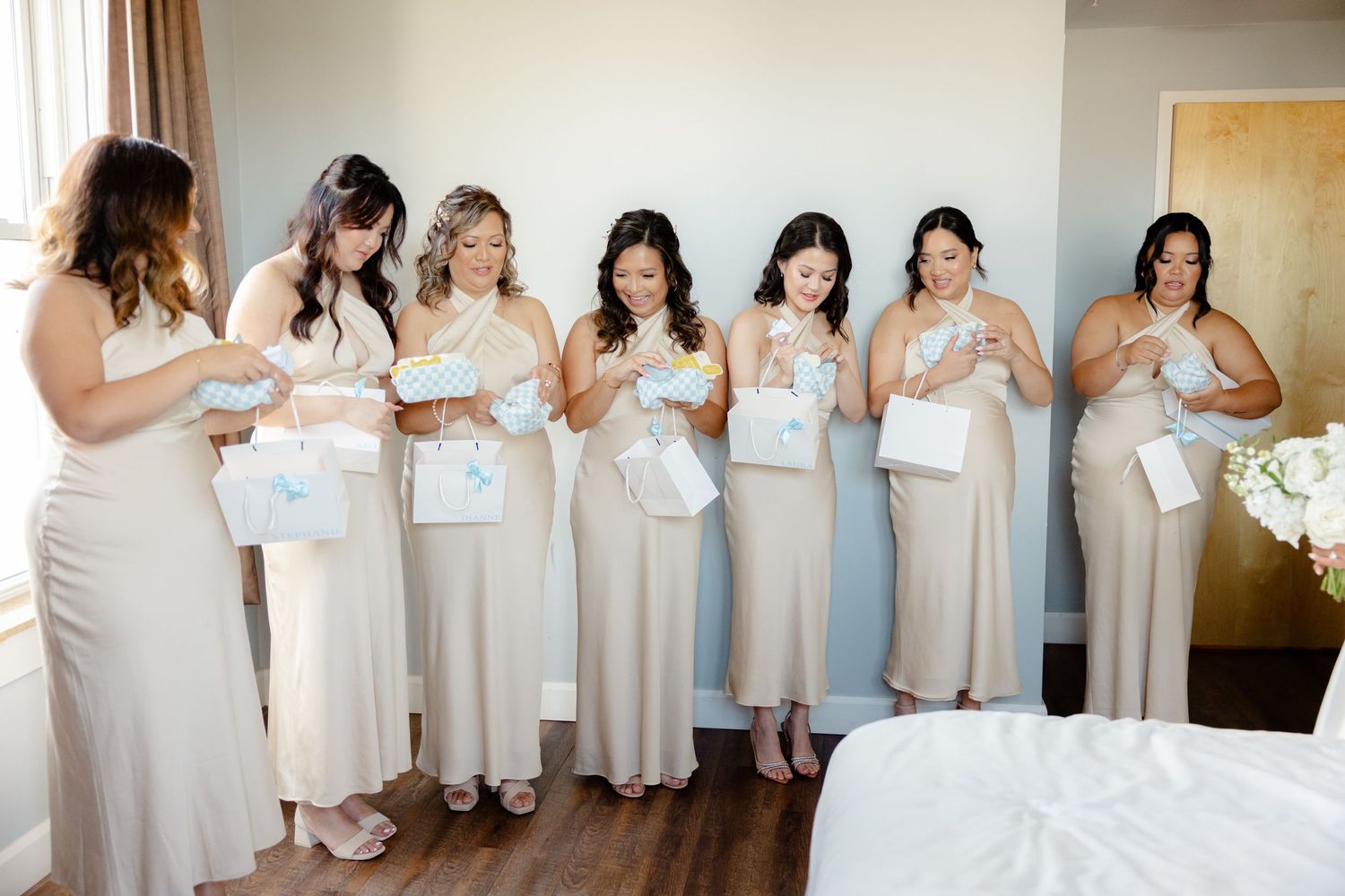Bridesmaids in champagne-colored dresses look at their phones during wedding preparations.