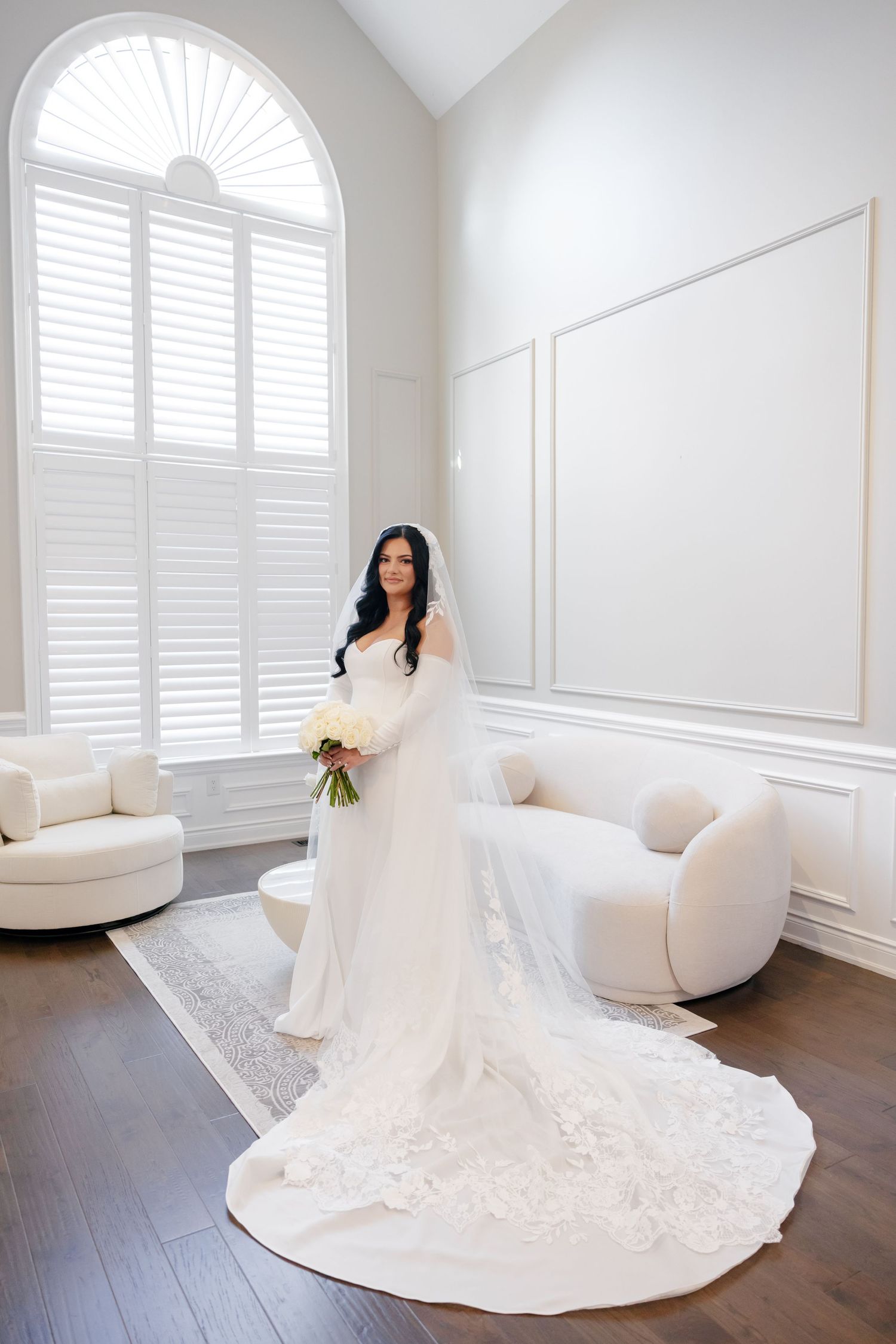 Elegant bridal portrait in bright white room with arched window and flowing train.