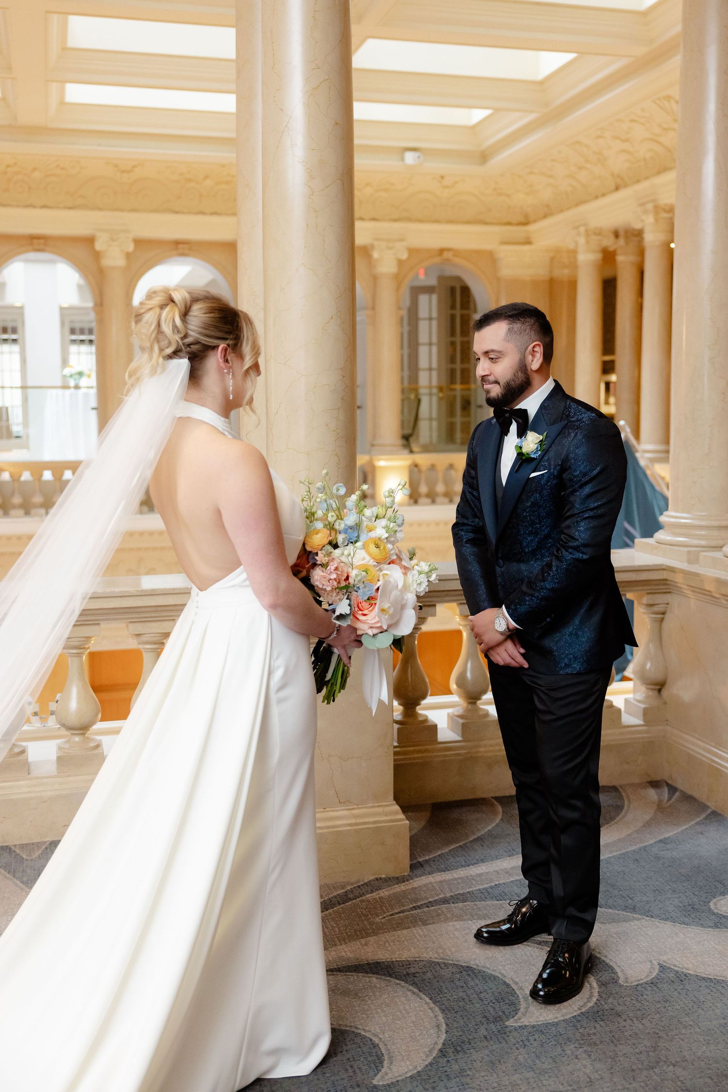 A wedding first look sequence showing a bride surprising the groom in an elegant columned hallway.