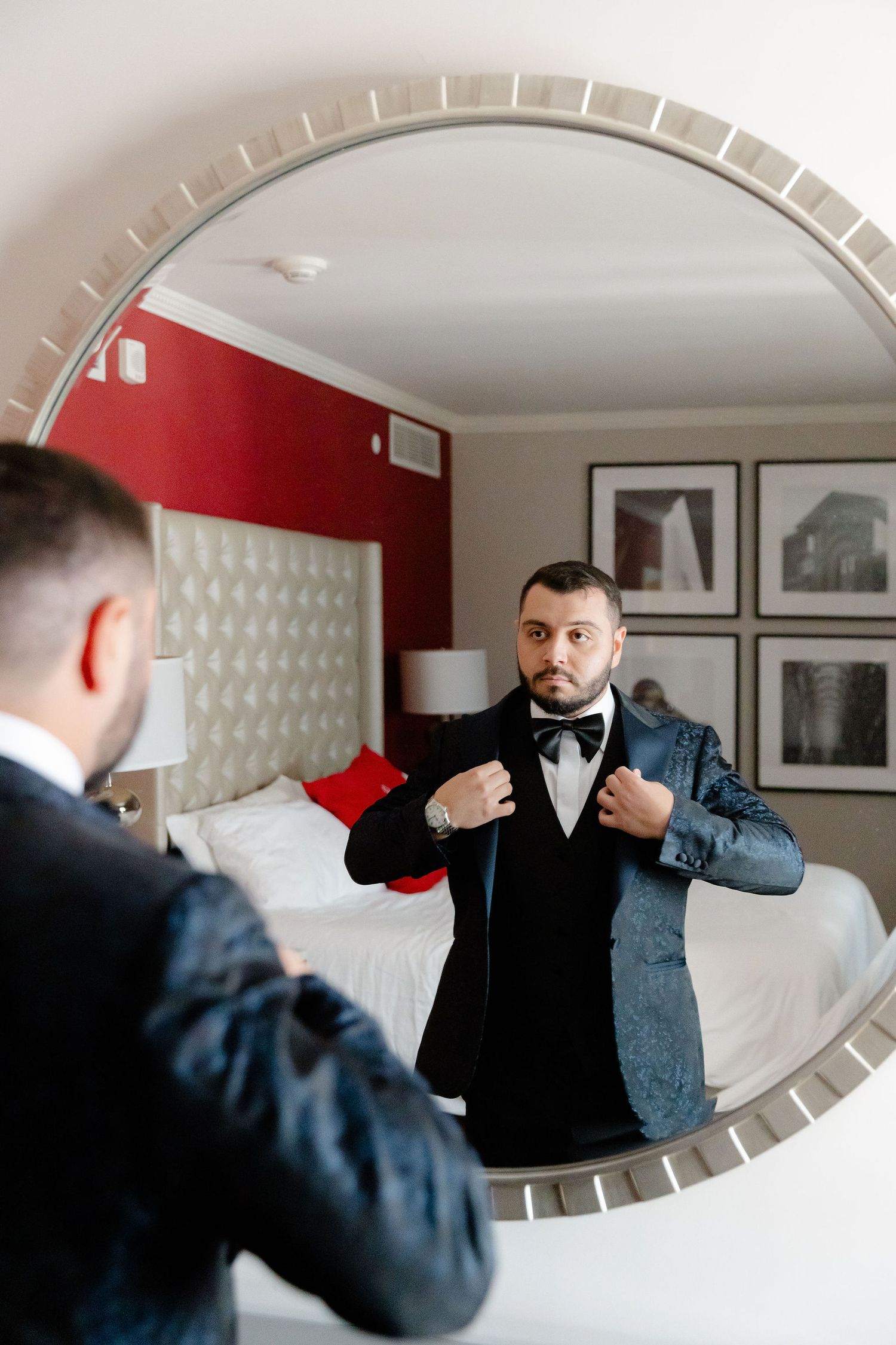 Series of shots showing someone fixing their tie while looking in an oval mirror mounted on a red wall.