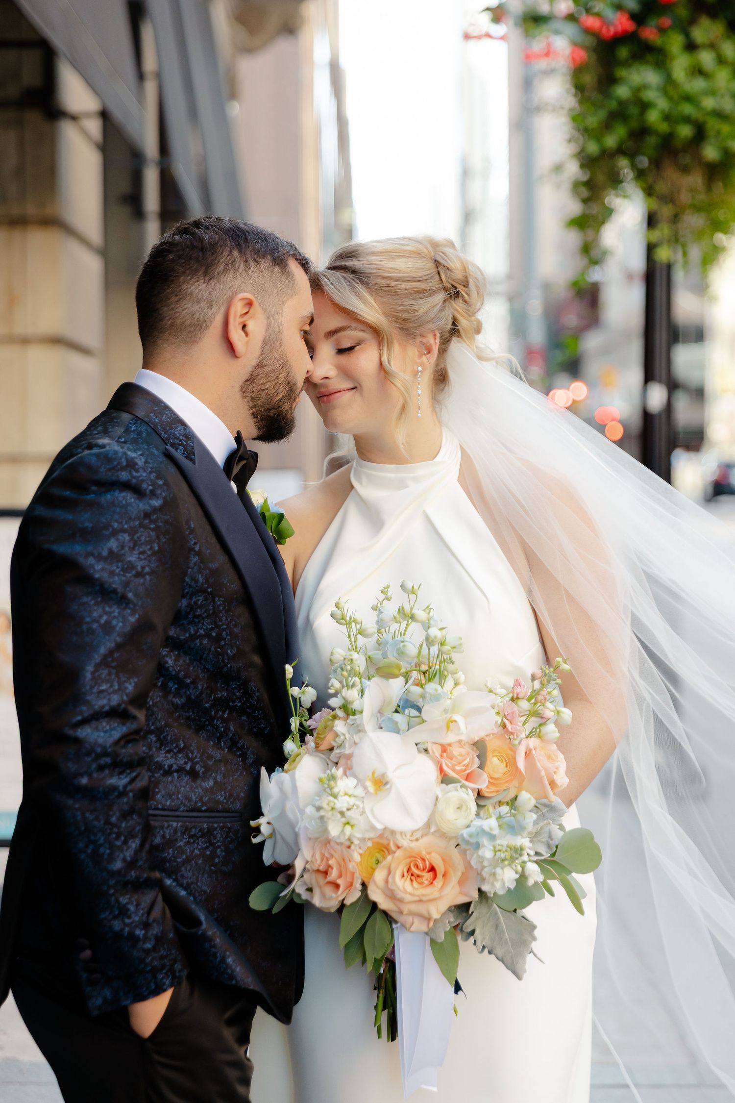 Romantic wedding couple shares intimate moments in elegant attire with peach and white floral bouquet.