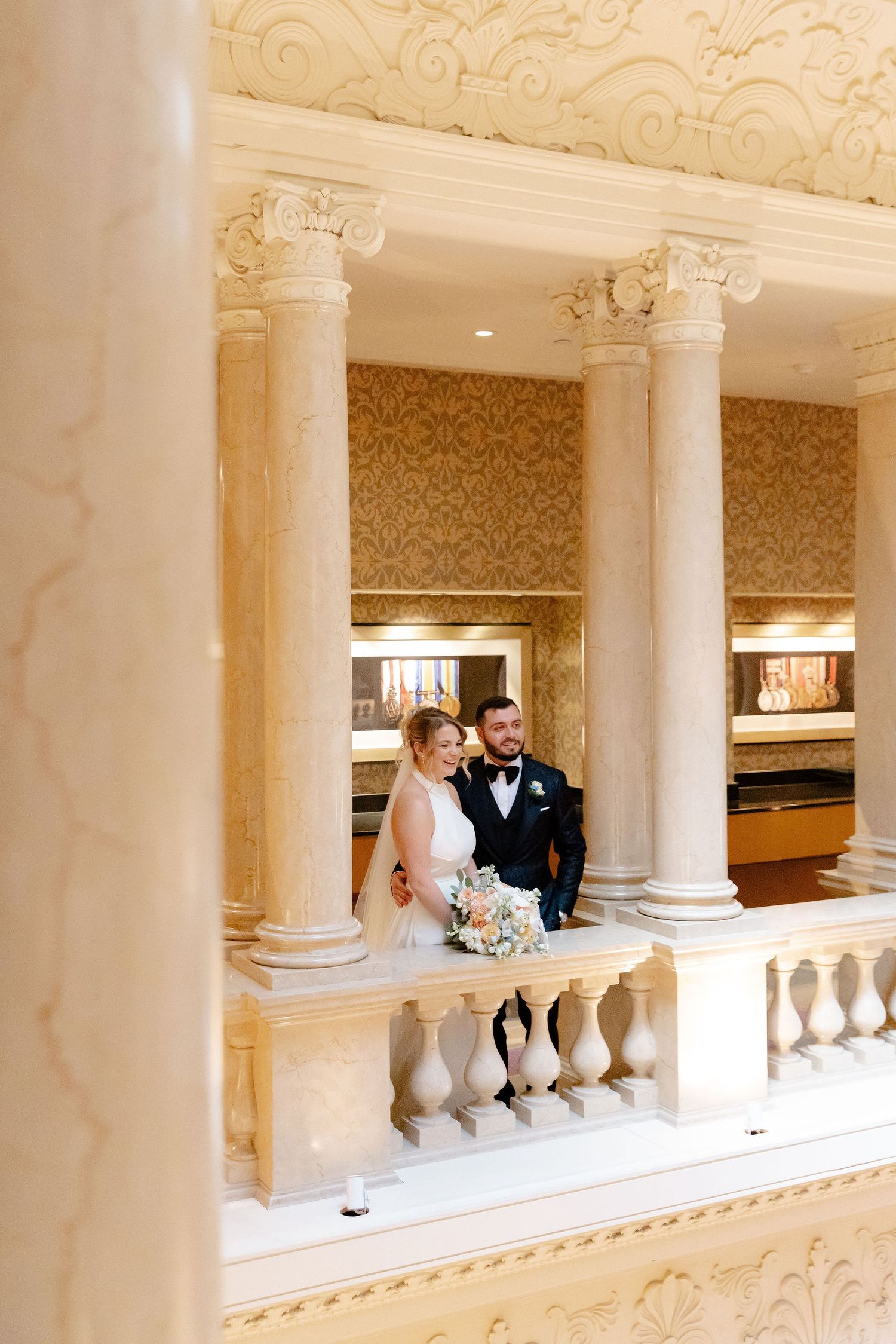 Classic wedding portraits captured along ornate interior balcony with white columns.