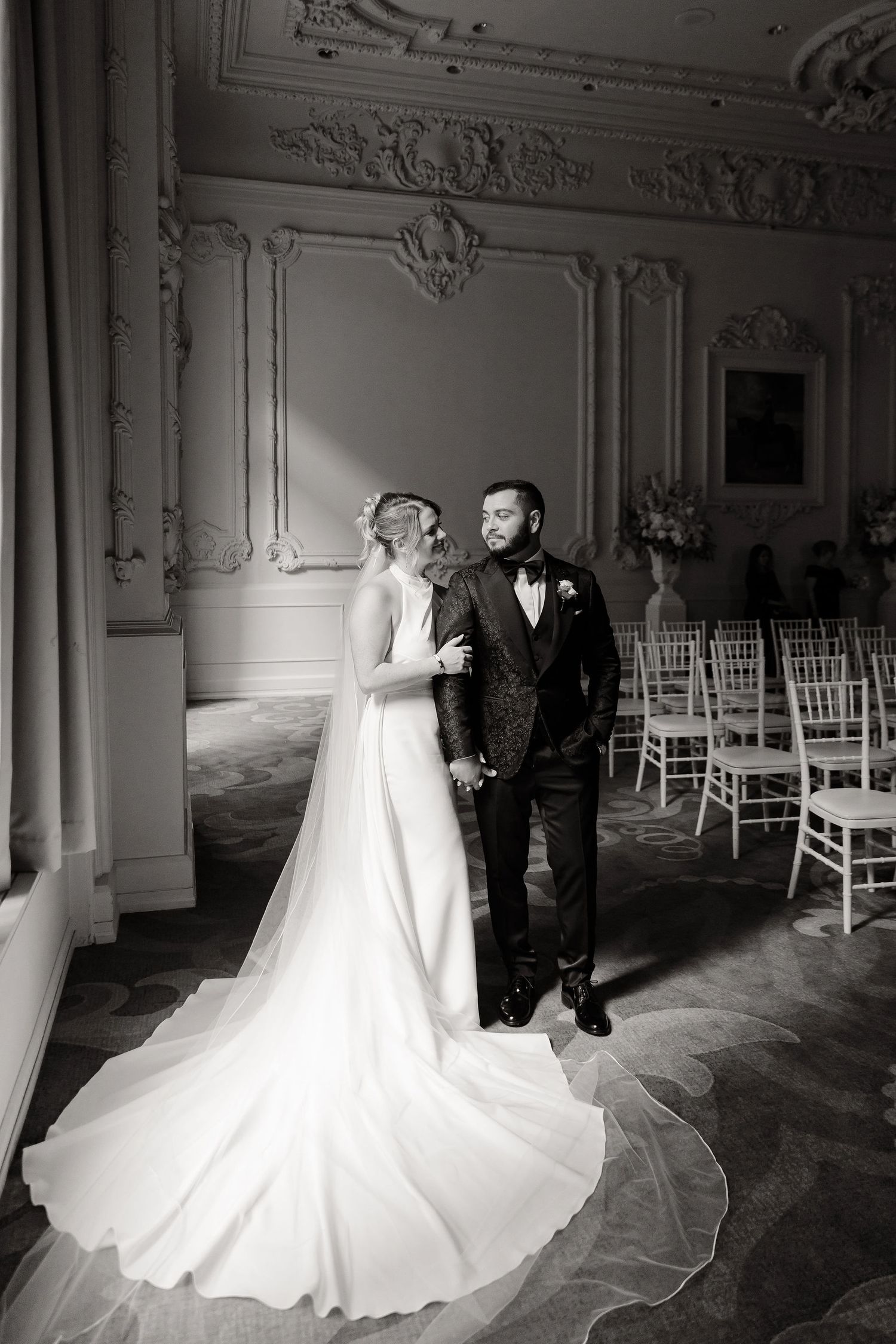 Black and white wedding photos showing a couple in an elegant ballroom with dramatic lighting and white chairs.