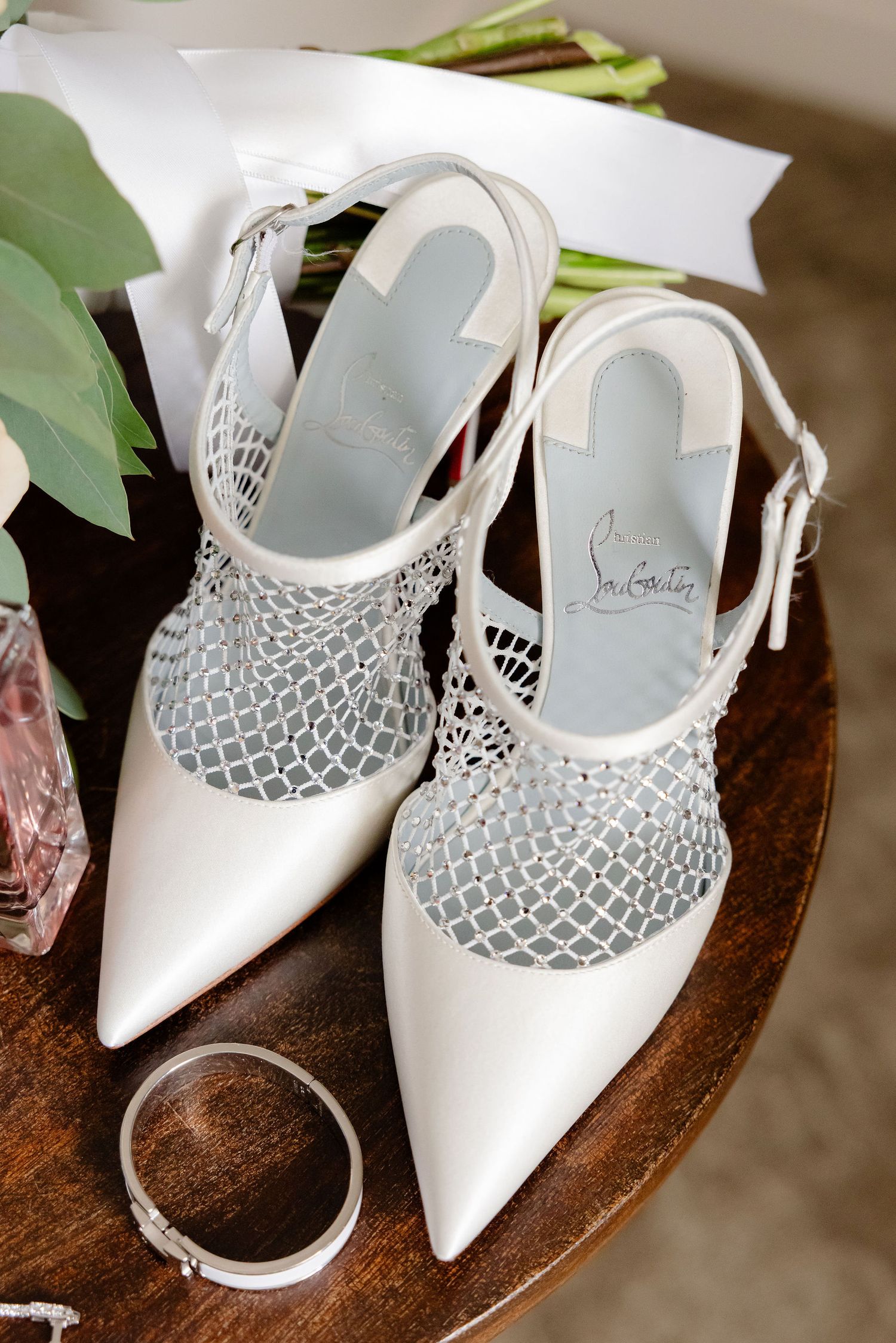 White bridal shoes with delicate mesh detailing displayed on a wooden surface.