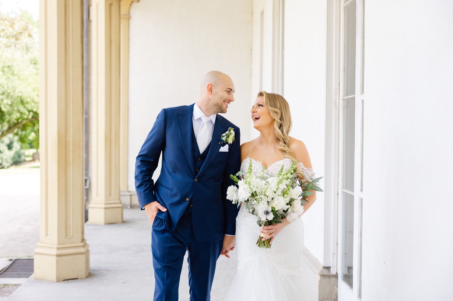 A cheerful wedding moment captured on a bright white porch with classic architectural details.
