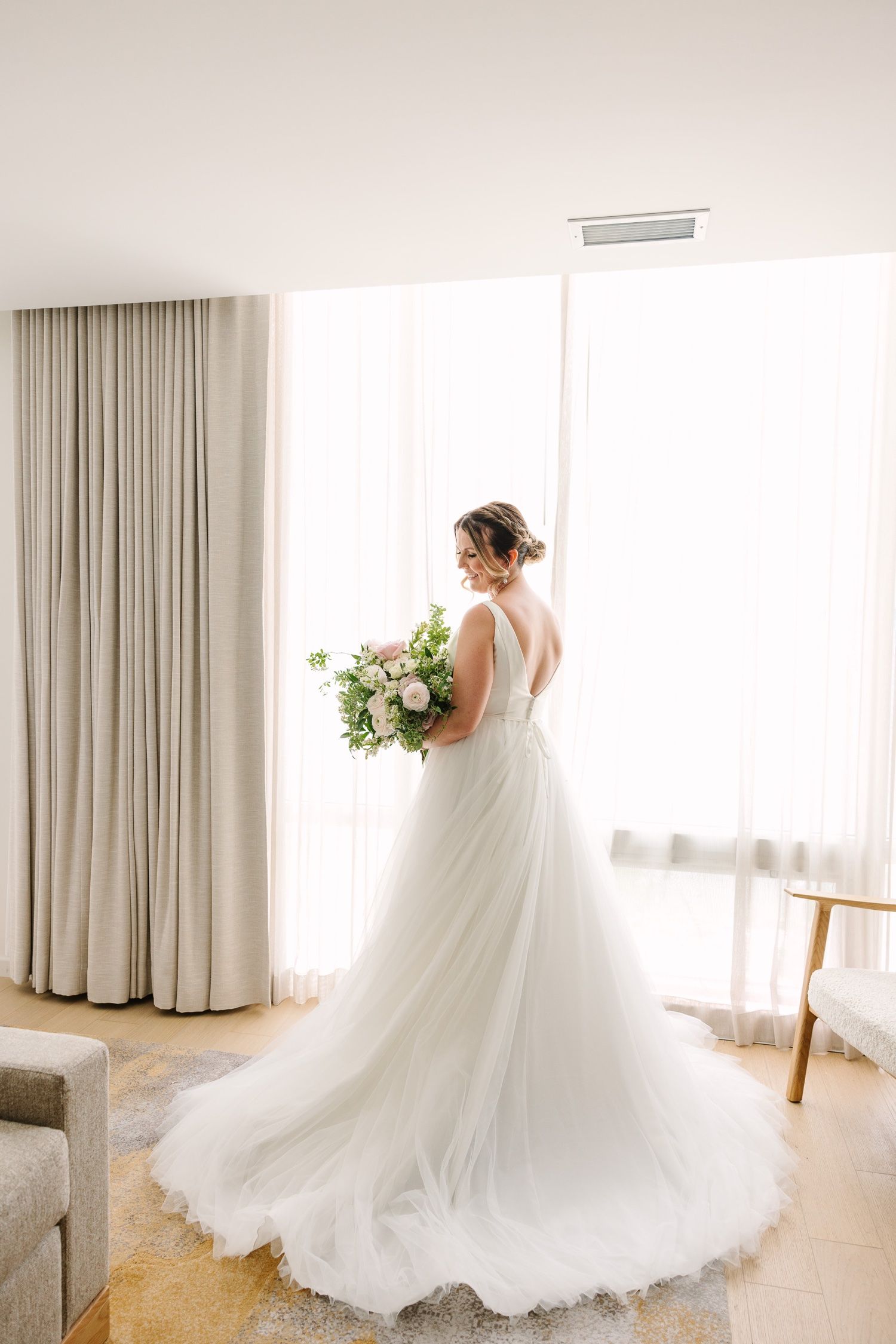 Back view of wedding dress showing elegant train and v-back detail in sunlit room.