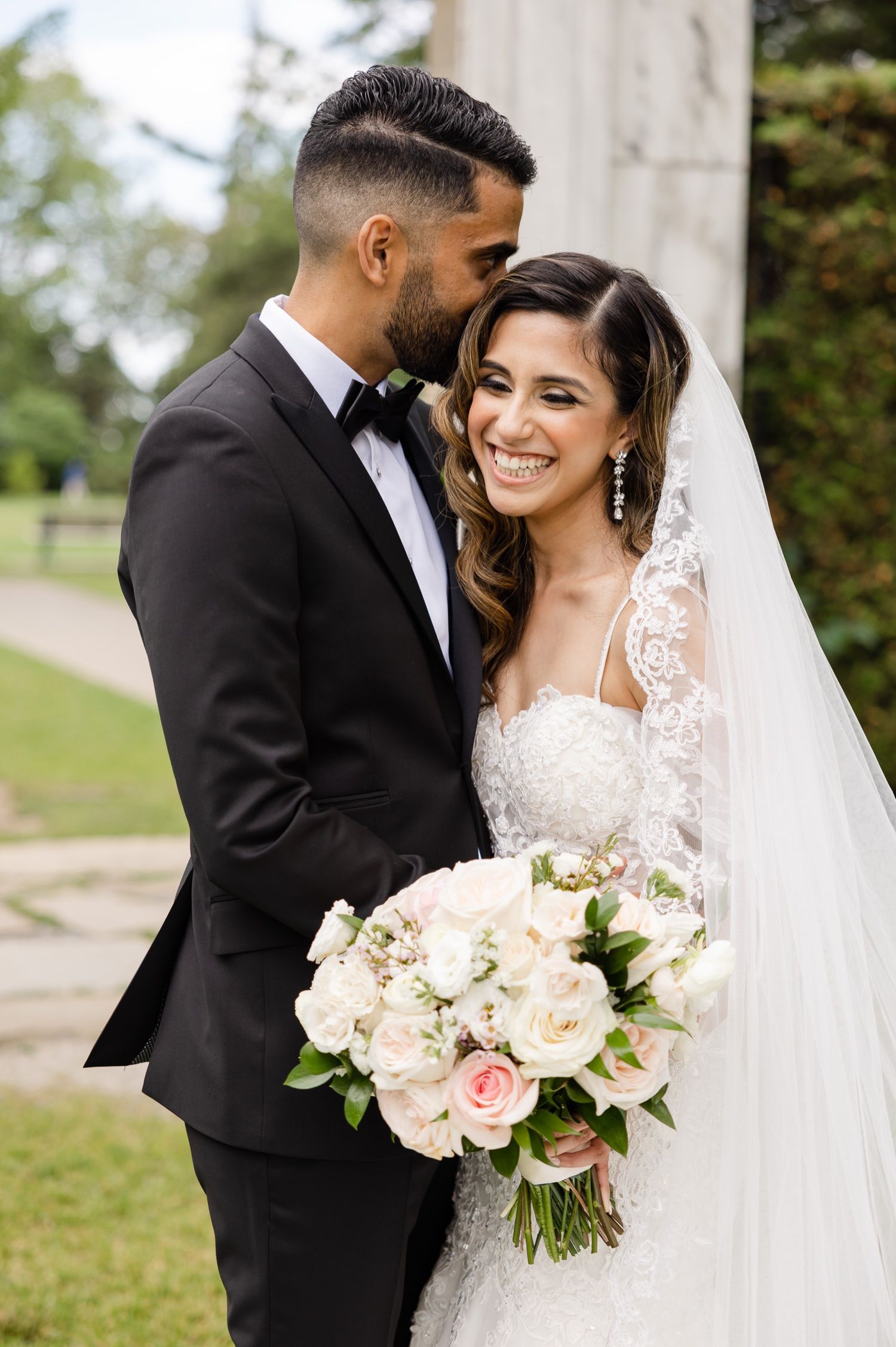 Joyful wedding moment captured with elegant bouquet of blush roses and cathedral veil.
