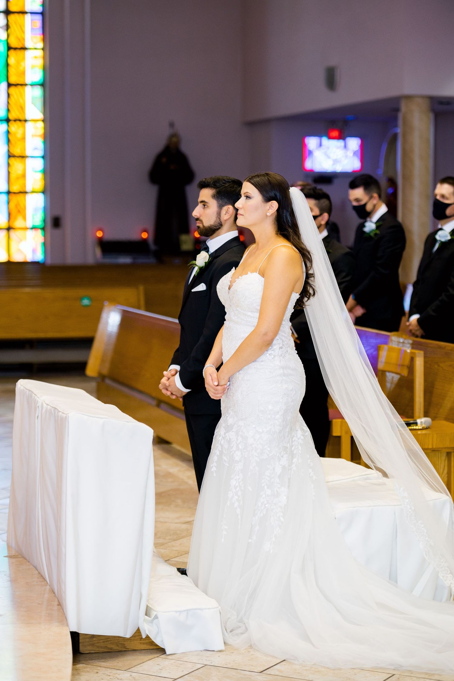 Wedding ceremony in progress with colorful stained glass windows and white decor.