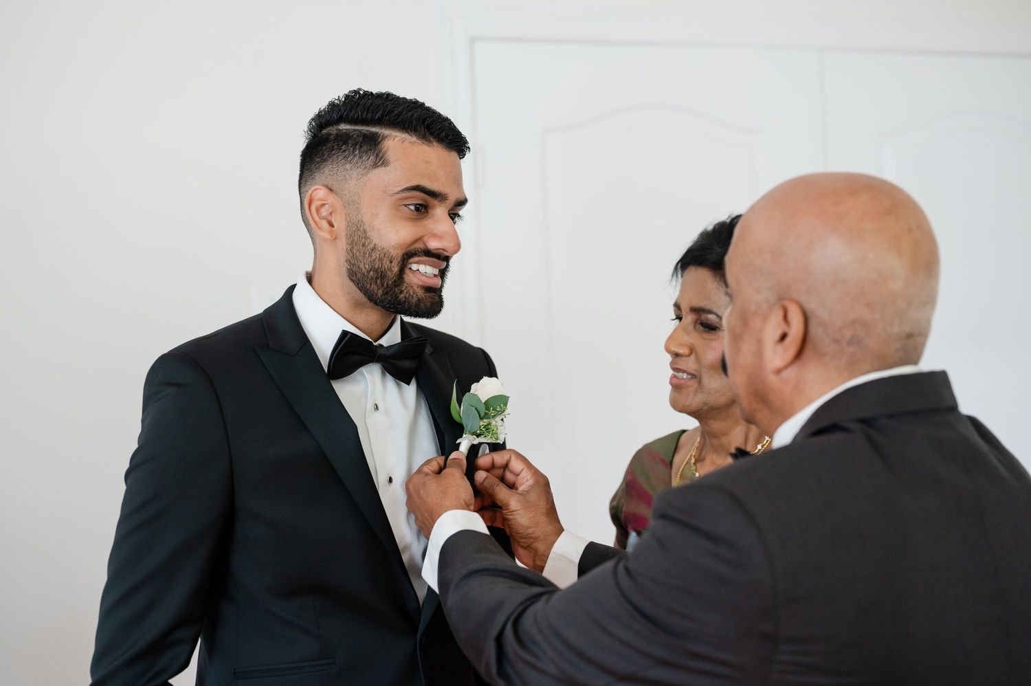 A tender moment of boutonniere pinning during wedding preparations in a bright room.